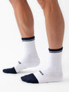 Person wearing white Essential Calf Socks from the Cozy Earth 2-Pack collection, standing on a white background. The socks feature a ribbed texture with the word "BOMBAS" written near the toes and have black toes and cuffs. |Color:Eclipse