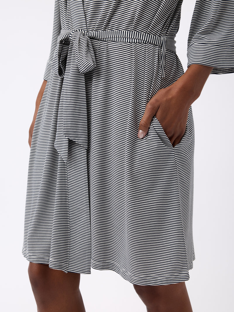 A person wears a knee-length, black and white Women's Bamboo Stretch-Knit Kimono Robe by Cozy Earth, featuring a waist belt and side pocket. The background is plain white.