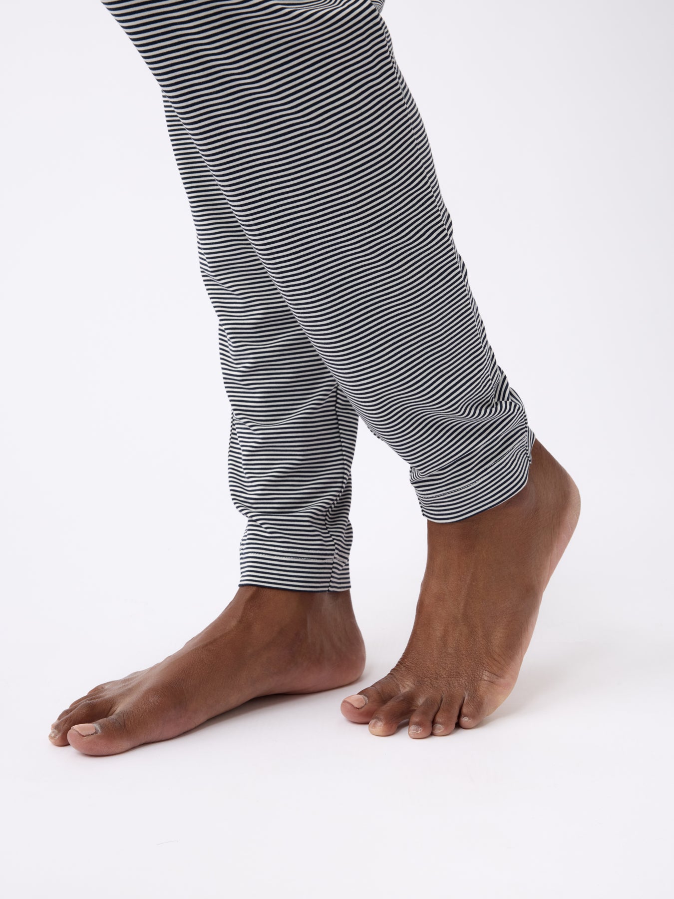 Bare feet step forward in Cozy Earth's Women's Bamboo Stretch-Knit Tapered Pant, featuring black and white stripes with rolled-up cuffs, set against a plain white background. 