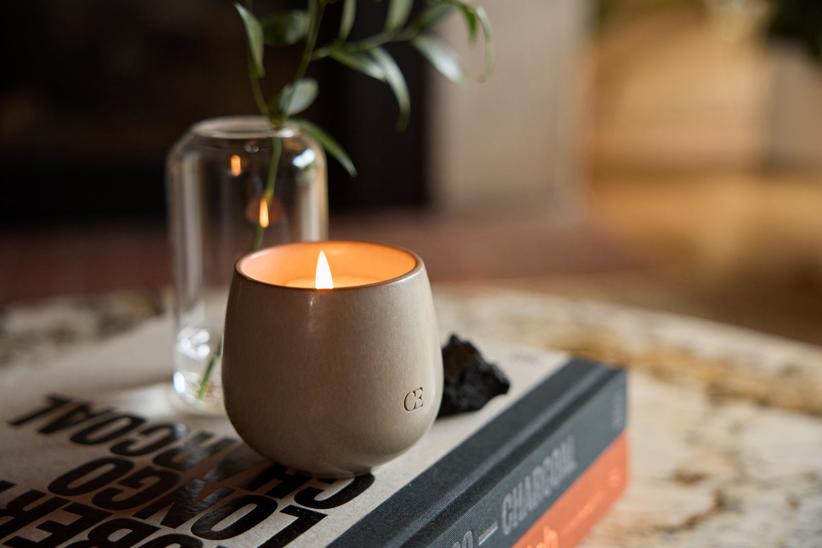 Cozy Earth Ember Candle lit on a coffee table next to a vase