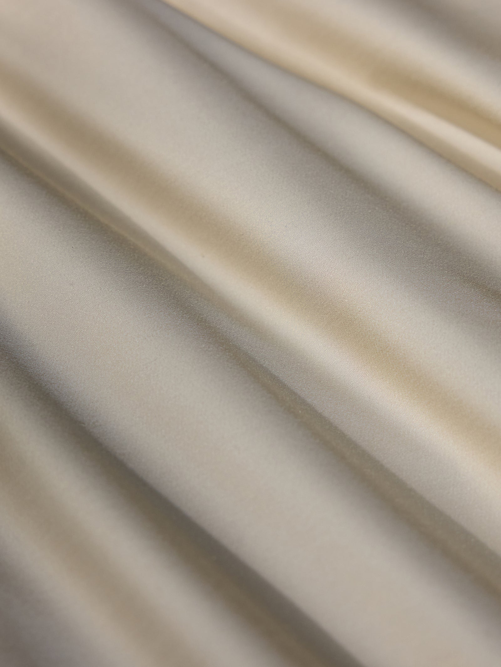 A close-up image of the Bamboo Duvet Cover from Cozy Earth, showcasing its smooth and silky beige fabric with gentle, soft folds. The material exudes a subtle sheen, creating a flowing and elegant texture. 