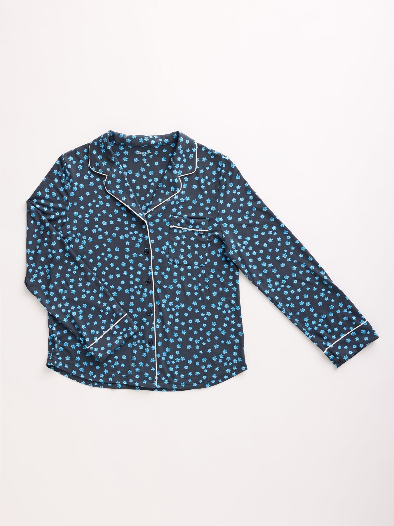 The Women's Bamboo Stretch-Knit Pajama Top by Cozy Earth features a dark blue and light blue floral pattern with white piping, a button-down front, long sleeves, and a notched collar, displayed flat on a white background. 