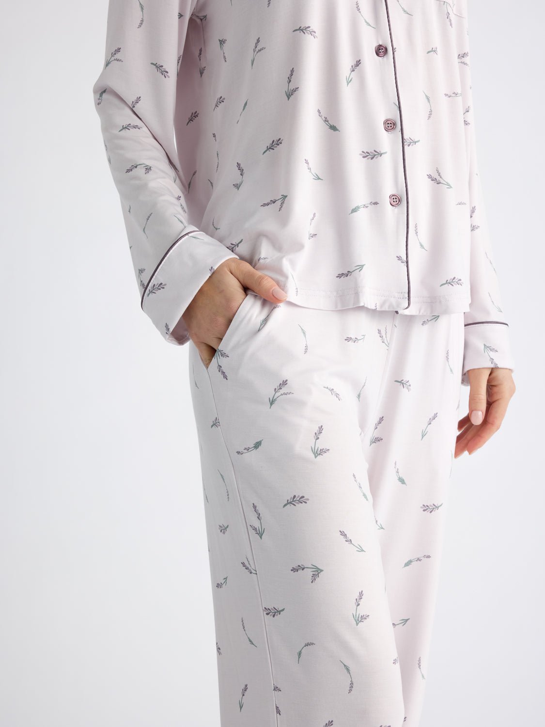 A person wears Cozy Earth Women's Bamboo Stretch-Knit Pajama Pants featuring a subtle branch pattern and matching pajama top with dark piping and buttons, with one hand in the pants pocket. The background is plain white. 