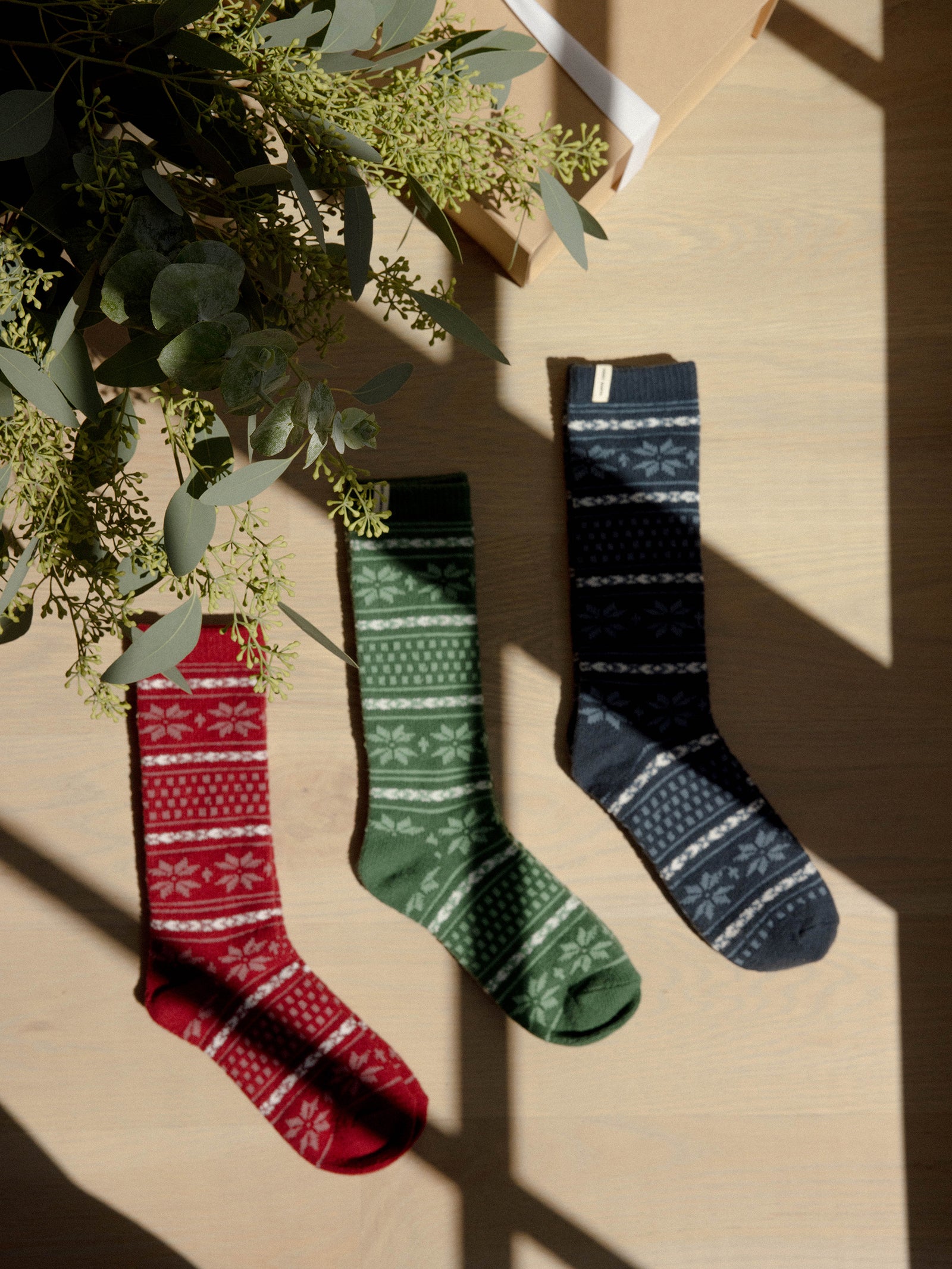 Snowflake Plush Lounge Socks in Garnet, Jade, and Eclipse lie under a Christmas tree. 