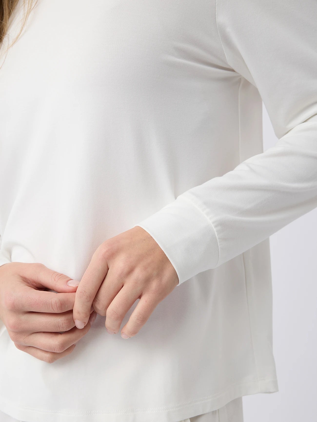 A woman adjusts the cuff of a Cozy Earth Women's Stretch Knit Bamboo Long Sleeve Lounge Tee against a neutral background. 