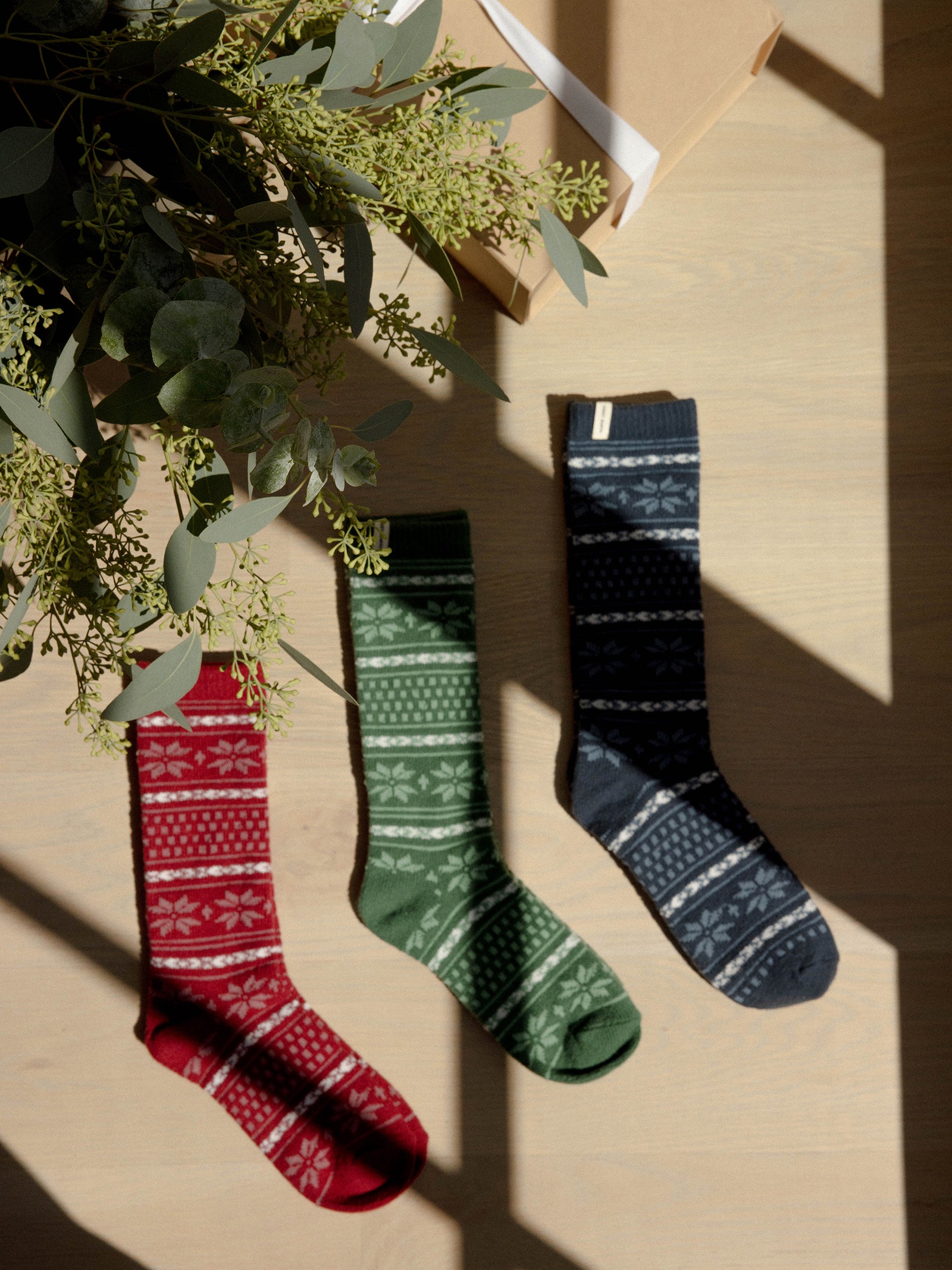 Snowflake Plush Lounge Socks in Garnet, Jade, and Eclipse lie under a Christmas tree. 