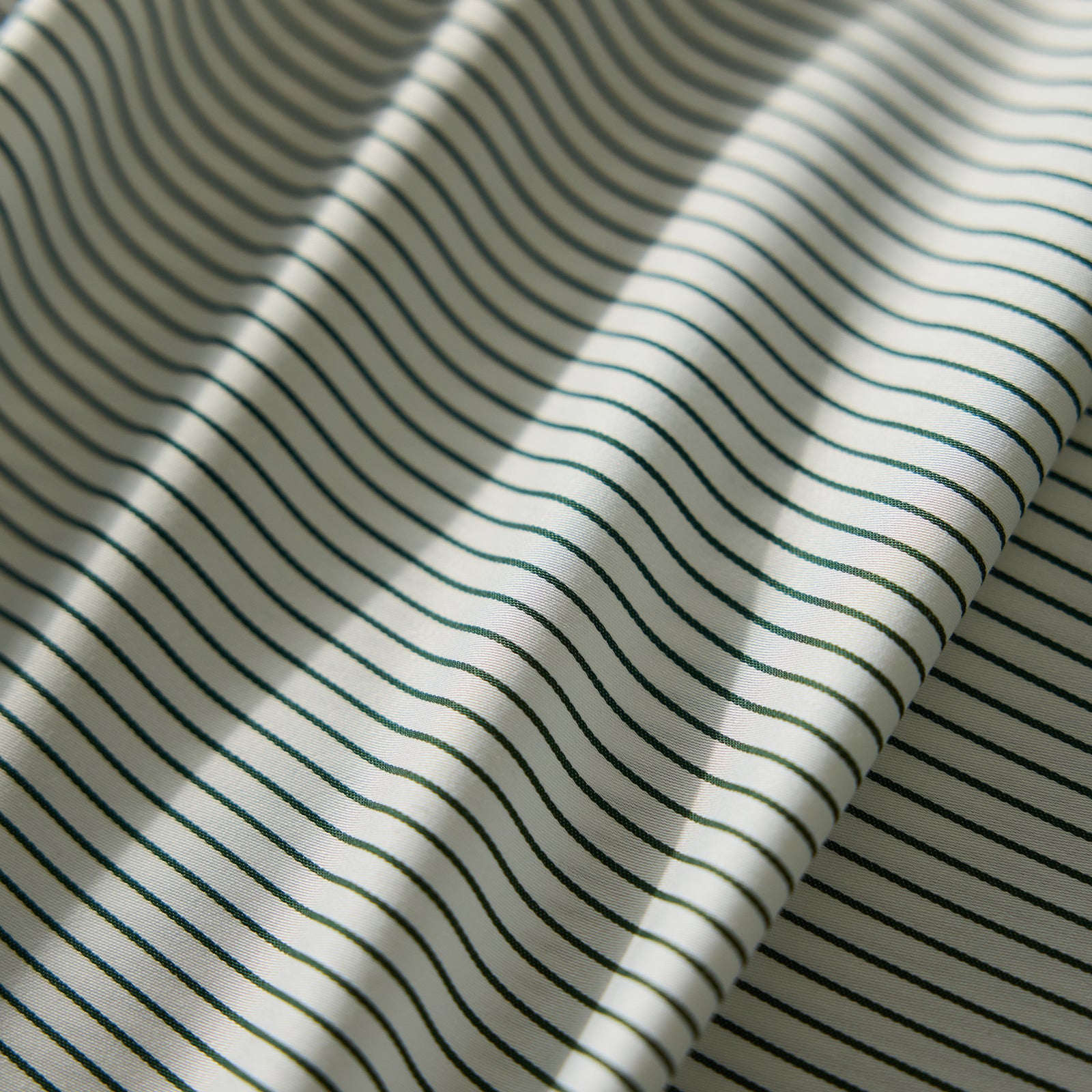 Close-up of the Bamboo Flat Sheet from Cozy Earth, featuring a cream-colored fabric with thin, evenly spaced black stripes. The sheet lies flat with gentle folds, creating soft shadows and highlights. 