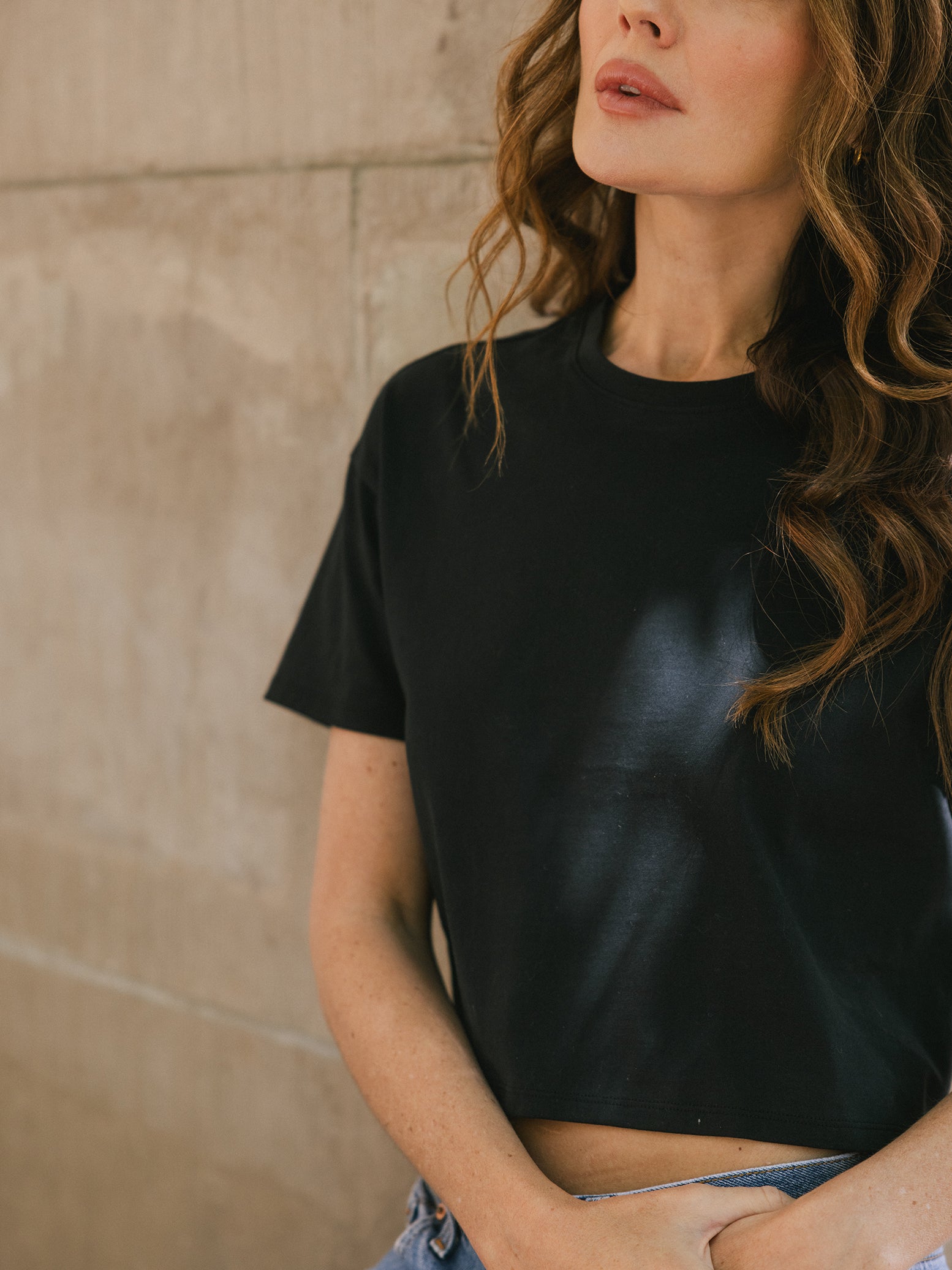 Jet Black All Day Cropped Tee. The photo of the All Day Cropped Tee is taken with a with a city style background and is worn by a woman. 