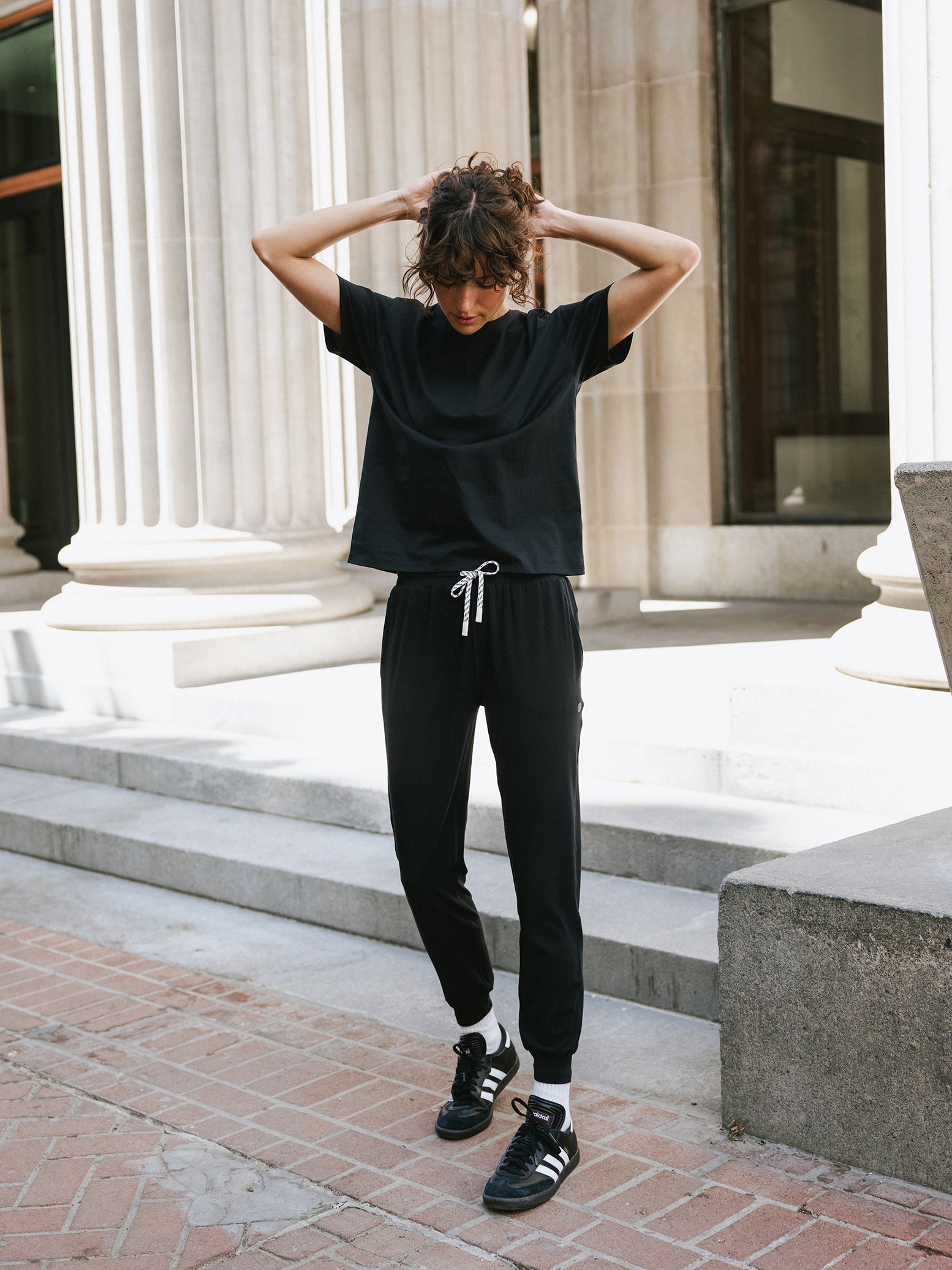 Jet Black Studio Jogger. The Studio Joggers are worn by a woman photographed with a city type background. 