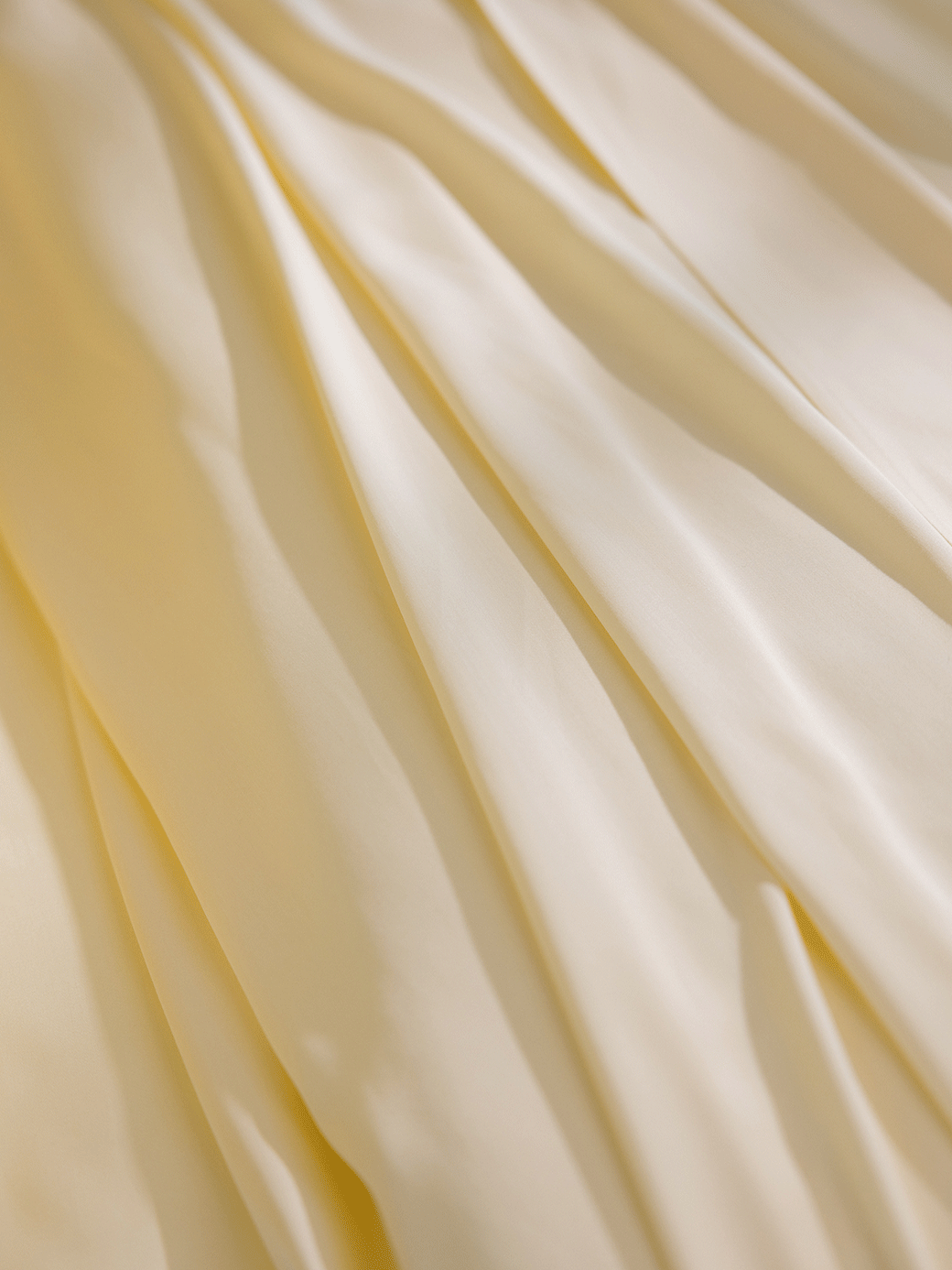 The Bamboo Fitted Sheet - Last Chance by Cozy Earth features smooth, cream-colored fabric with soft folds and gentle shadows for an elegant, luxurious look. Silky and lightweight, the sheet is bathed in warm, diffused lighting.