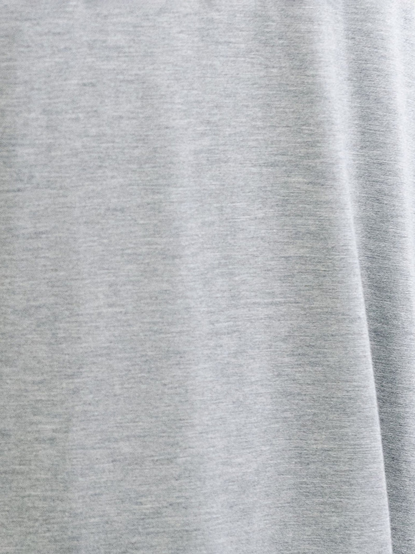 A close-up view of the light gray fabric in the Men's Stretch-Knit Short Sleeve Bamboo Pajama Set by Cozy Earth reveals a smooth texture. The fabric displays a slight heathered appearance with subtle variations in shade, creating a soft and uniform pattern.