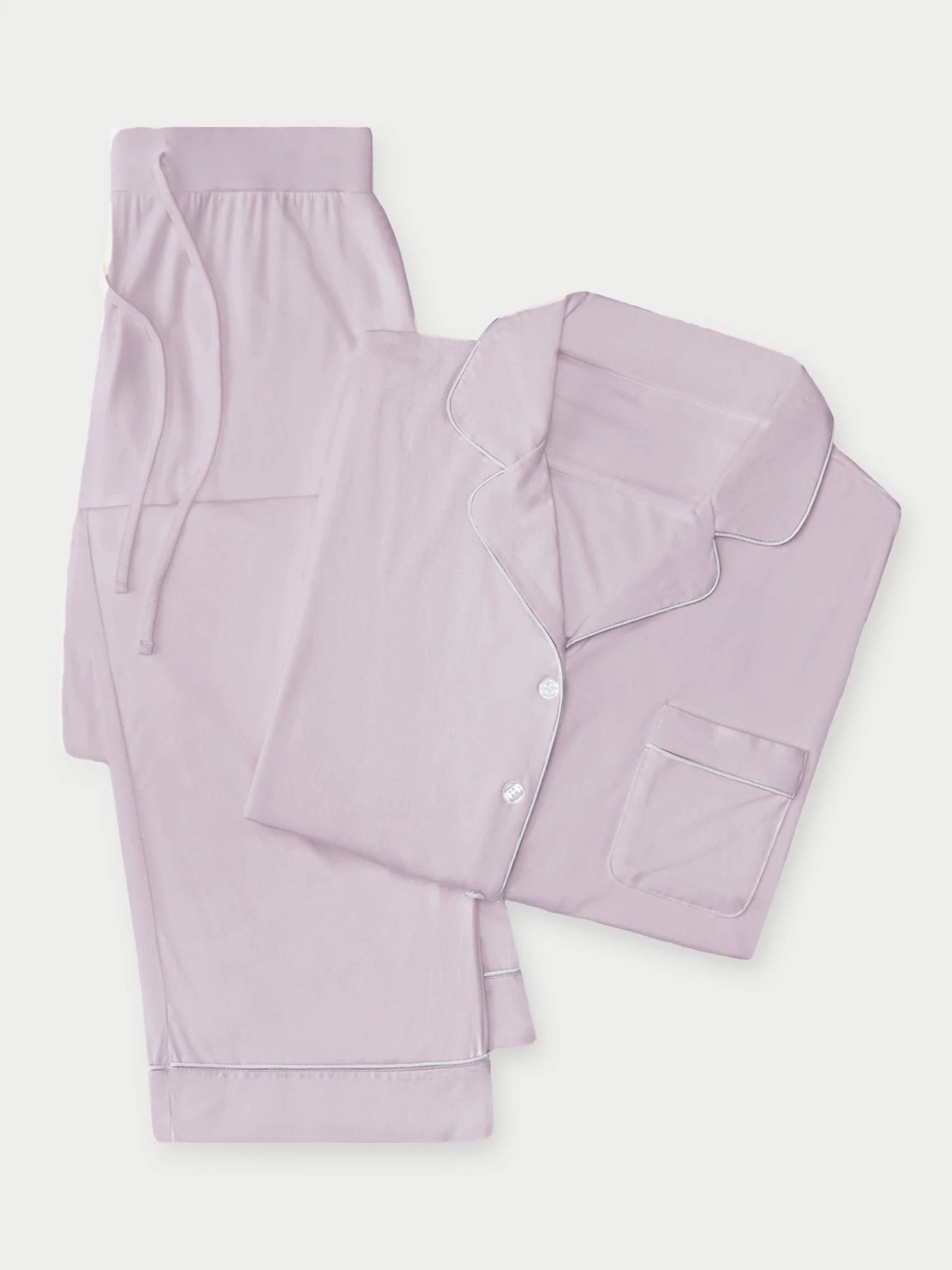 The Bedtime Bundle by Cozy Earth is a neatly folded set of matching light lavender pajamas, featuring a button-up top with a chest pocket and piping detail, paired with drawstring pants, all displayed against a plain white background.