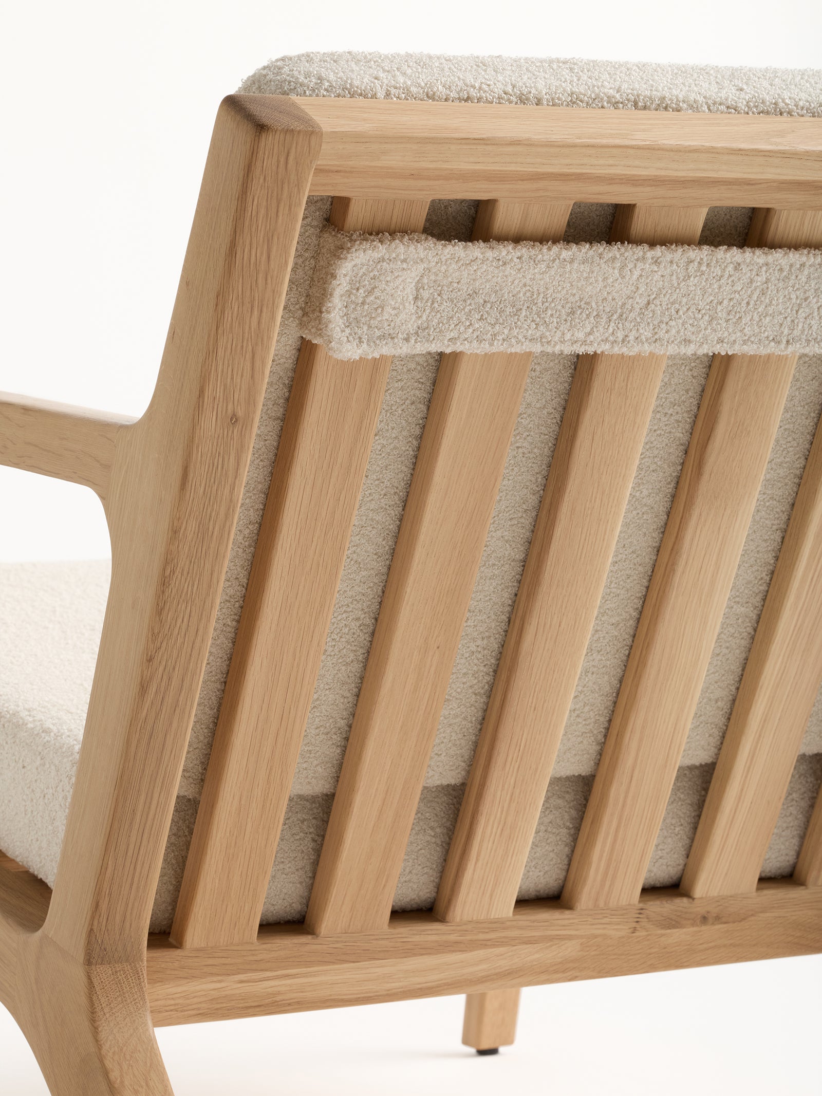 A close-up view of the Coronado Lounge Chair by Cozy Earth reveals its minimalist and natural design, featuring vertical wooden slats, a plush cream-colored cushion, and padded armrests. 