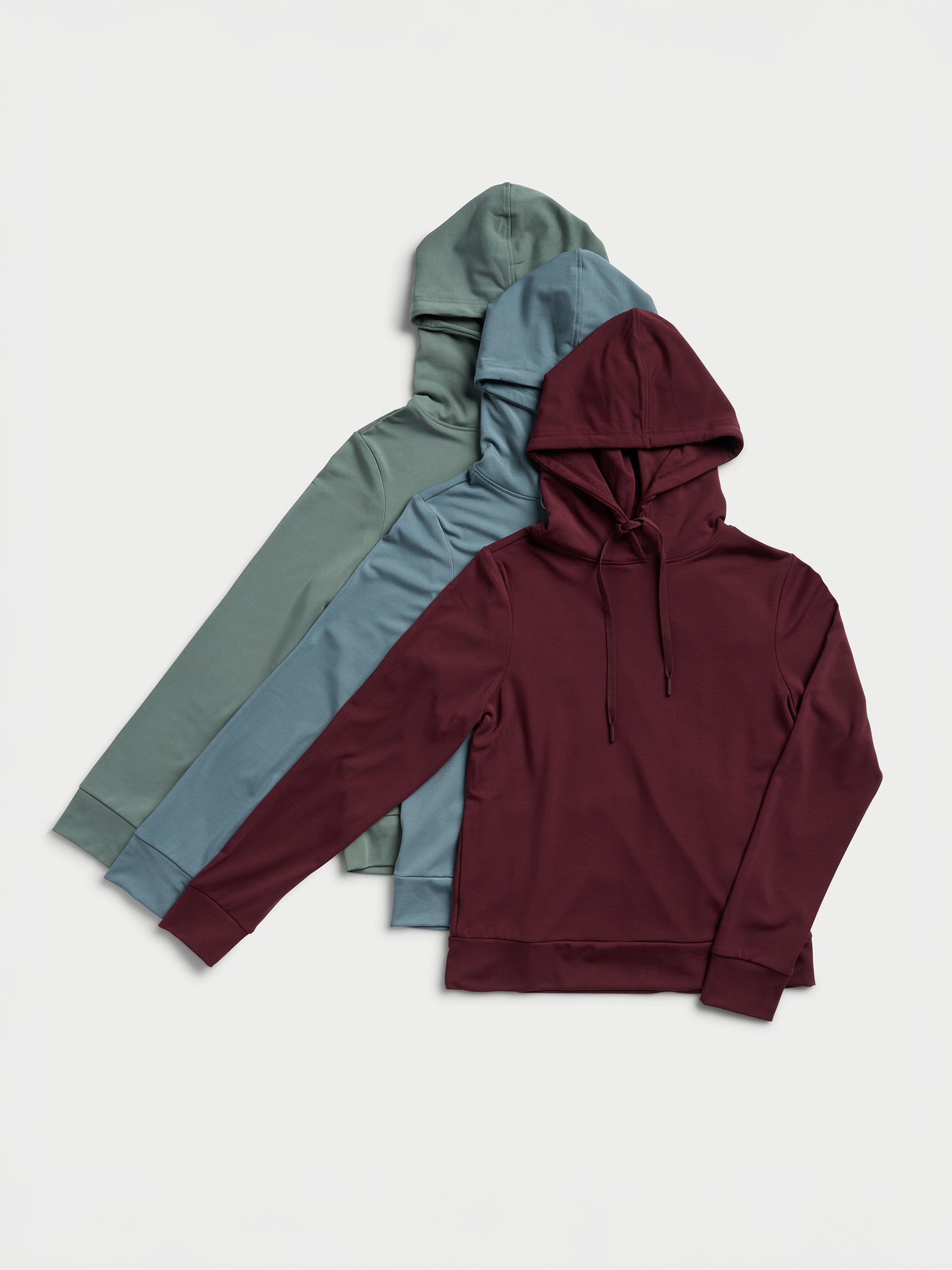 Four Women's Ultra-Soft Bamboo Hoodies by Cozy Earth are lined up on a light background. These hoodies come in a range of colors: burgundy, teal, blue, and green. Featuring drawstrings and long sleeves, they are displayed neatly overlapping each other. 