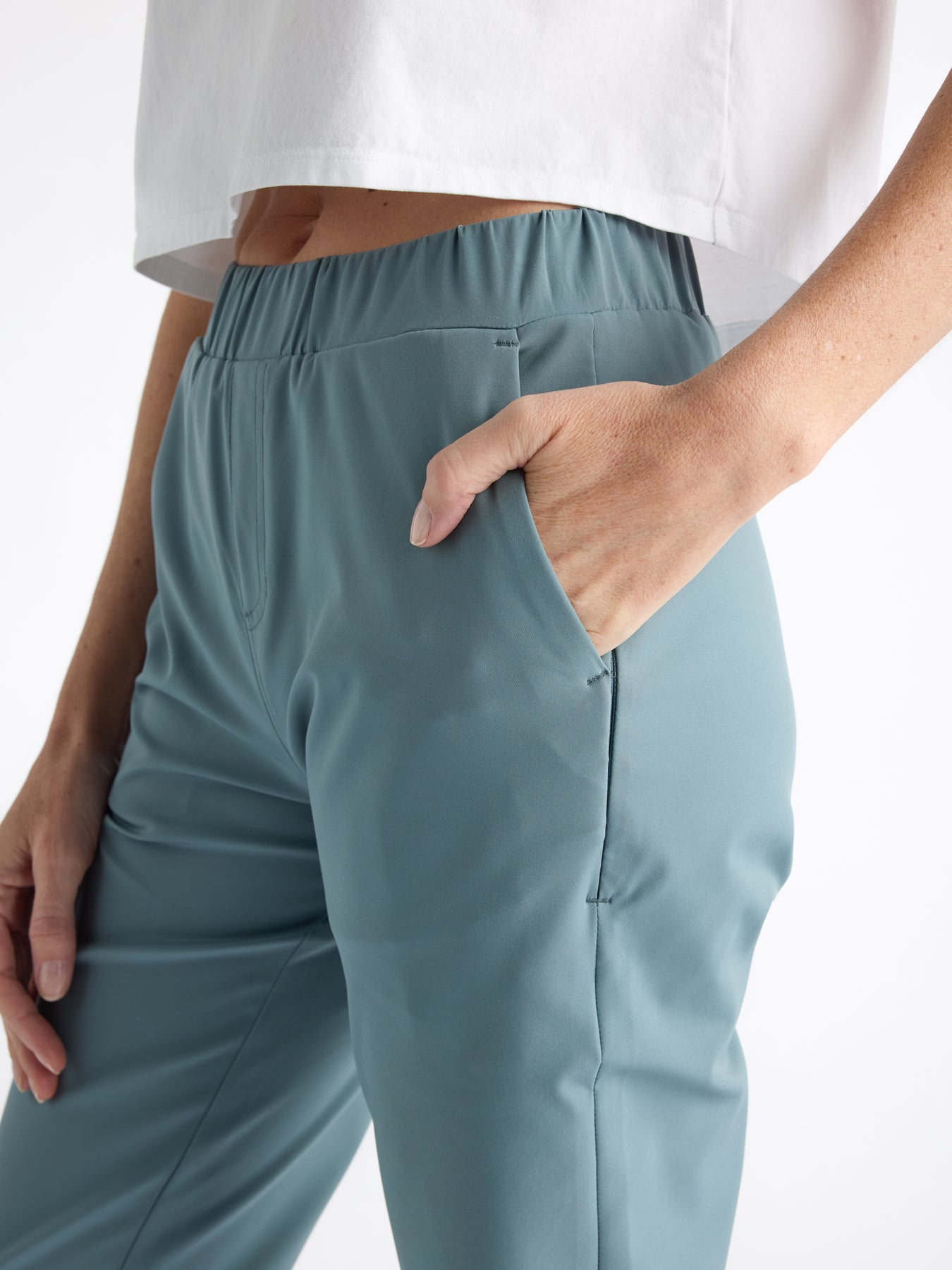 The person is wearing Cozy Earth's Women's Always Cropped Pant in light blue with hands in the pockets, paired with a white cropped short-sleeve top, set against a plain white background. 