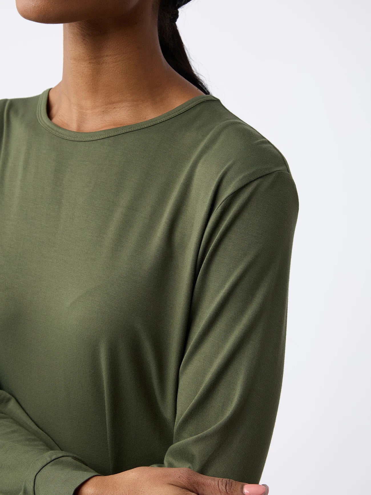 A woman wearing a Cozy Earth Women's Stretch Knit Bamboo Long Sleeve Lounge Tee in olive green stands with arms crossed, facing left against a plain white background. 