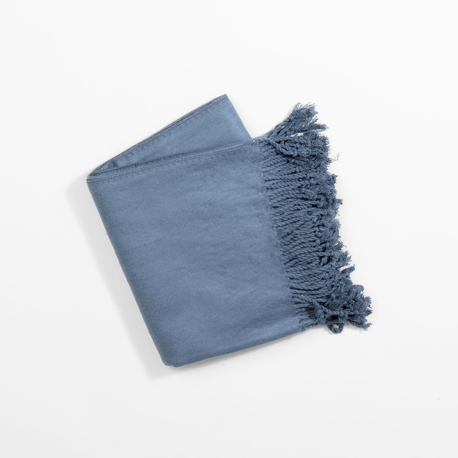 The Bamboo Tassel Throw from Cozy Earth, a folded and soft blue blanket featuring dense, decorative fringed edges on one side, is displayed against a plain white background. 