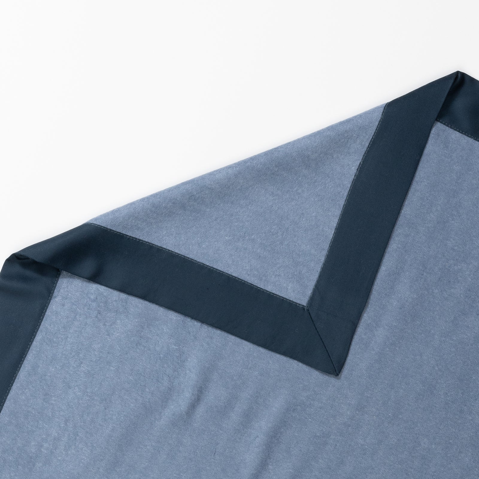 A close-up of a folded Cozy Earth Bamboo Blanket, featuring a light blue fabric with a dark blue border. The corner of the soft and smooth blanket is visible against a white background. 