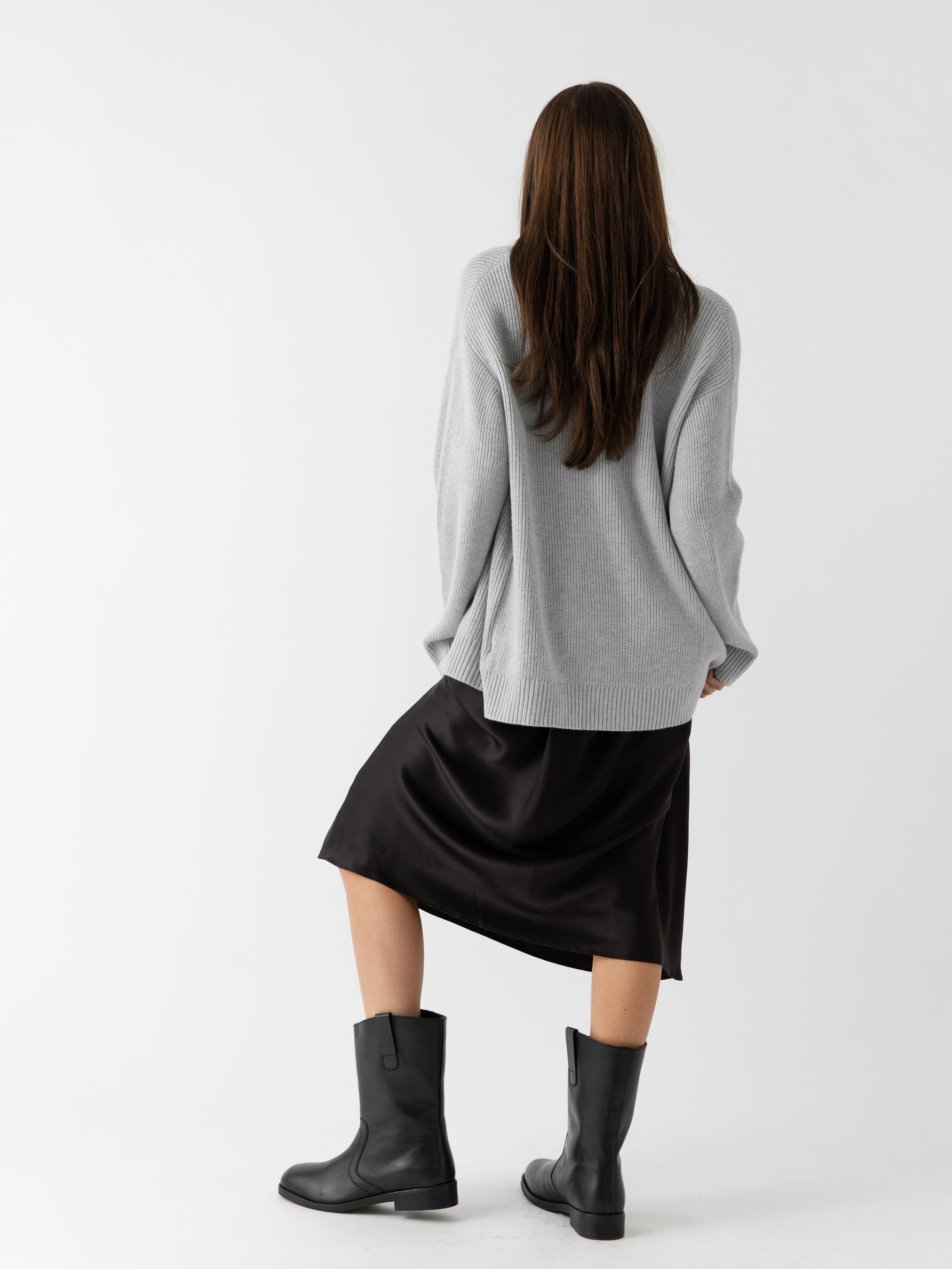 A woman wearing Cozy Earth Classic Cardigan in grey stands in front of a white background. She faces away from the camera 