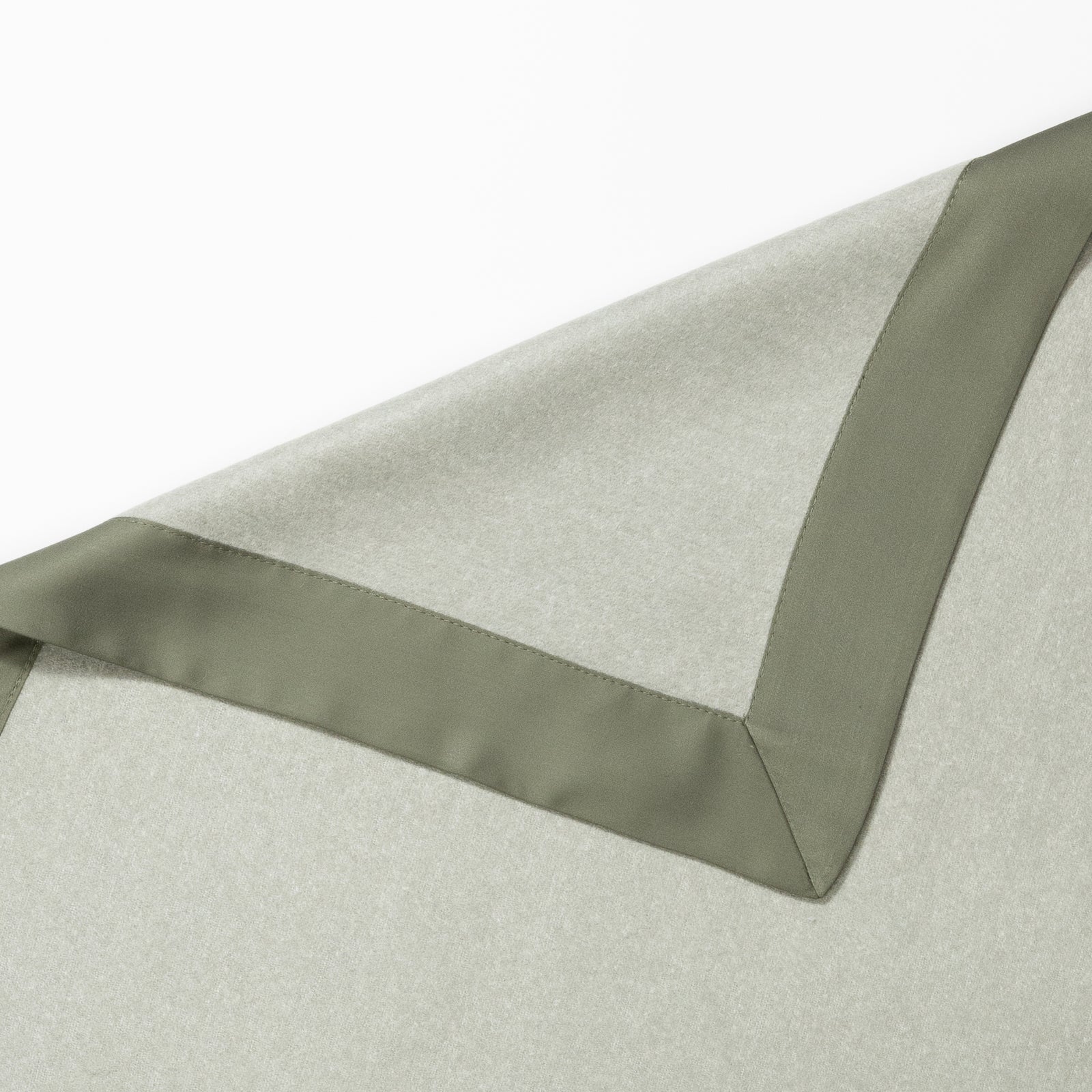 Close-up of a green and light gray Bamboo Blanket by Cozy Earth with a satin border. The upper part of the image shows the edge of the blanket, highlighting the smooth texture and sleek design of the border. The fabric appears soft and finely woven. 