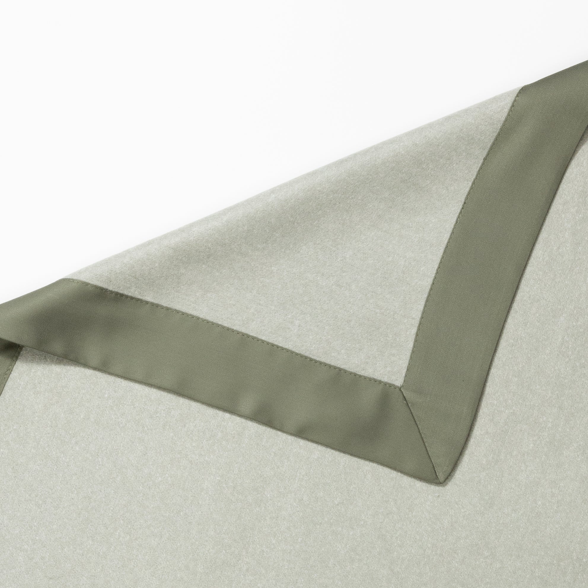 Close-up of a green and light gray Bamboo Blanket by Cozy Earth with a satin border. The upper part of the image shows the edge of the blanket, highlighting the smooth texture and sleek design of the border. The fabric appears soft and finely woven. |Color:Sage/Olive