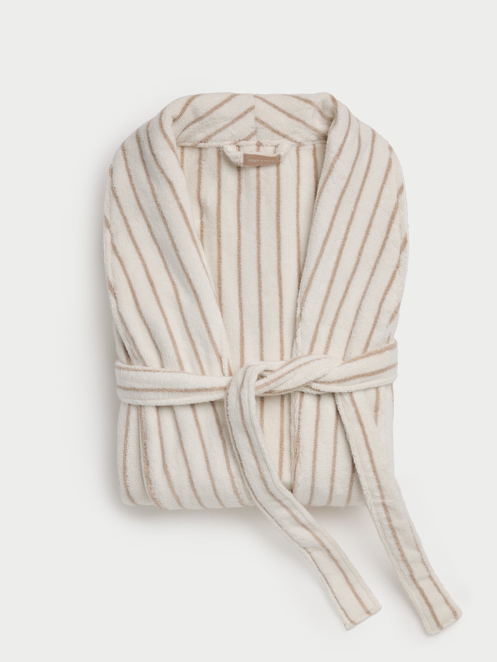 The Luxe Bath Robe by Cozy Earth is a folded, plush bathrobe with beige and white vertical stripes, featuring a shawl collar and tied with a matching belt. 