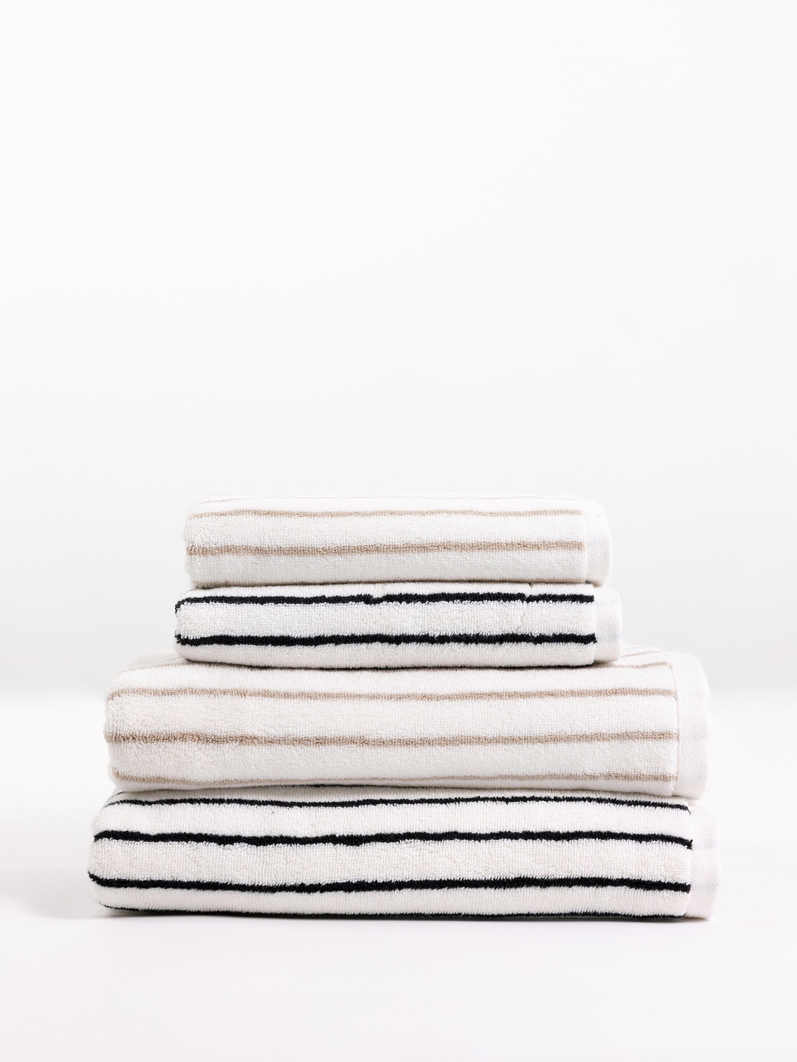 A set of neatly folded Luxe Bath Towels from Cozy Earth is stacked against a plain white background. The towels feature black and beige stripes on a white base. 