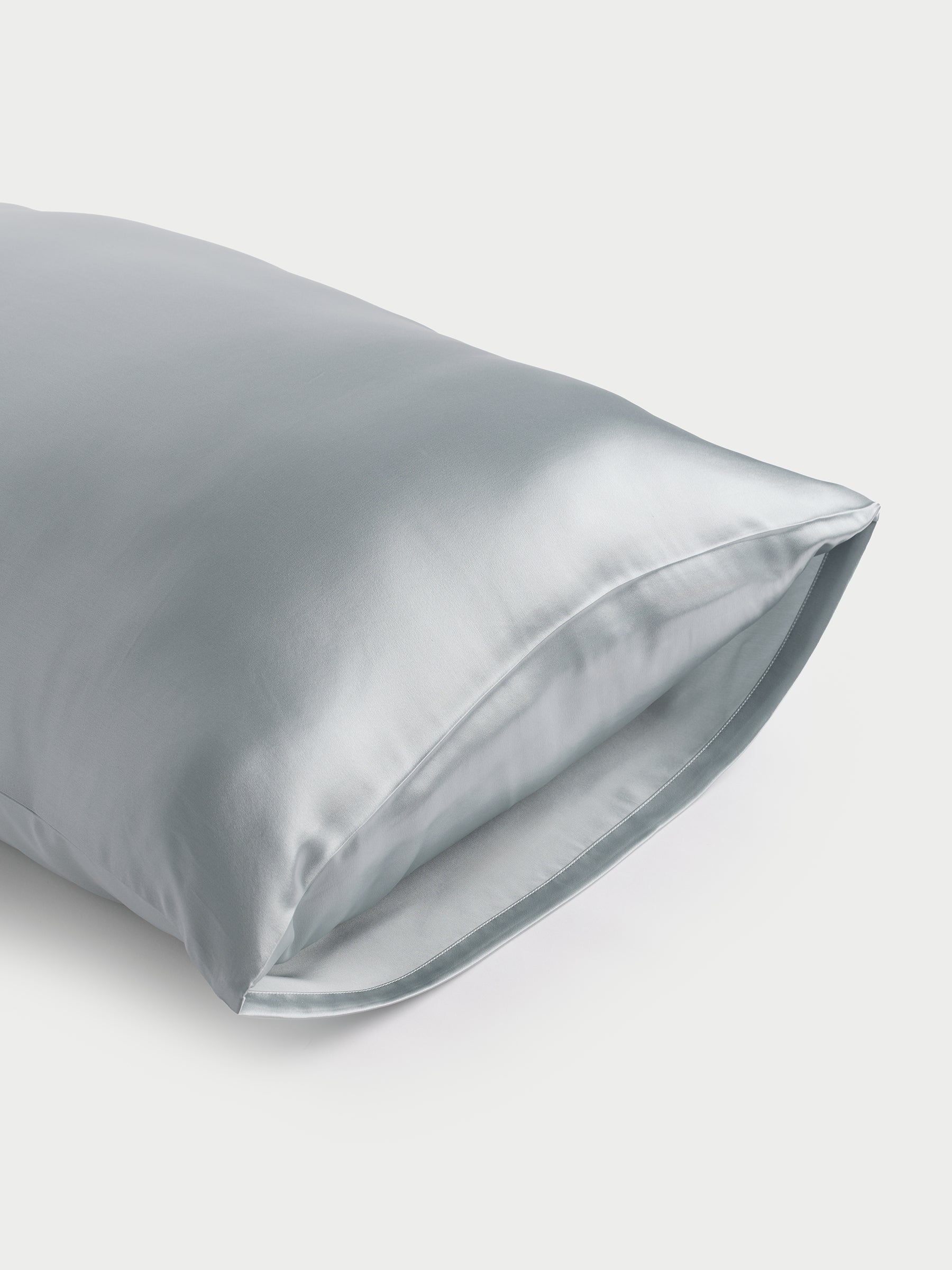 A shiny, light blue Silk Pillowcase by Cozy Earth with a smooth texture is displayed against a plain background. The open end is visible, highlighting the fabric's glossy finish. |Color:Shore