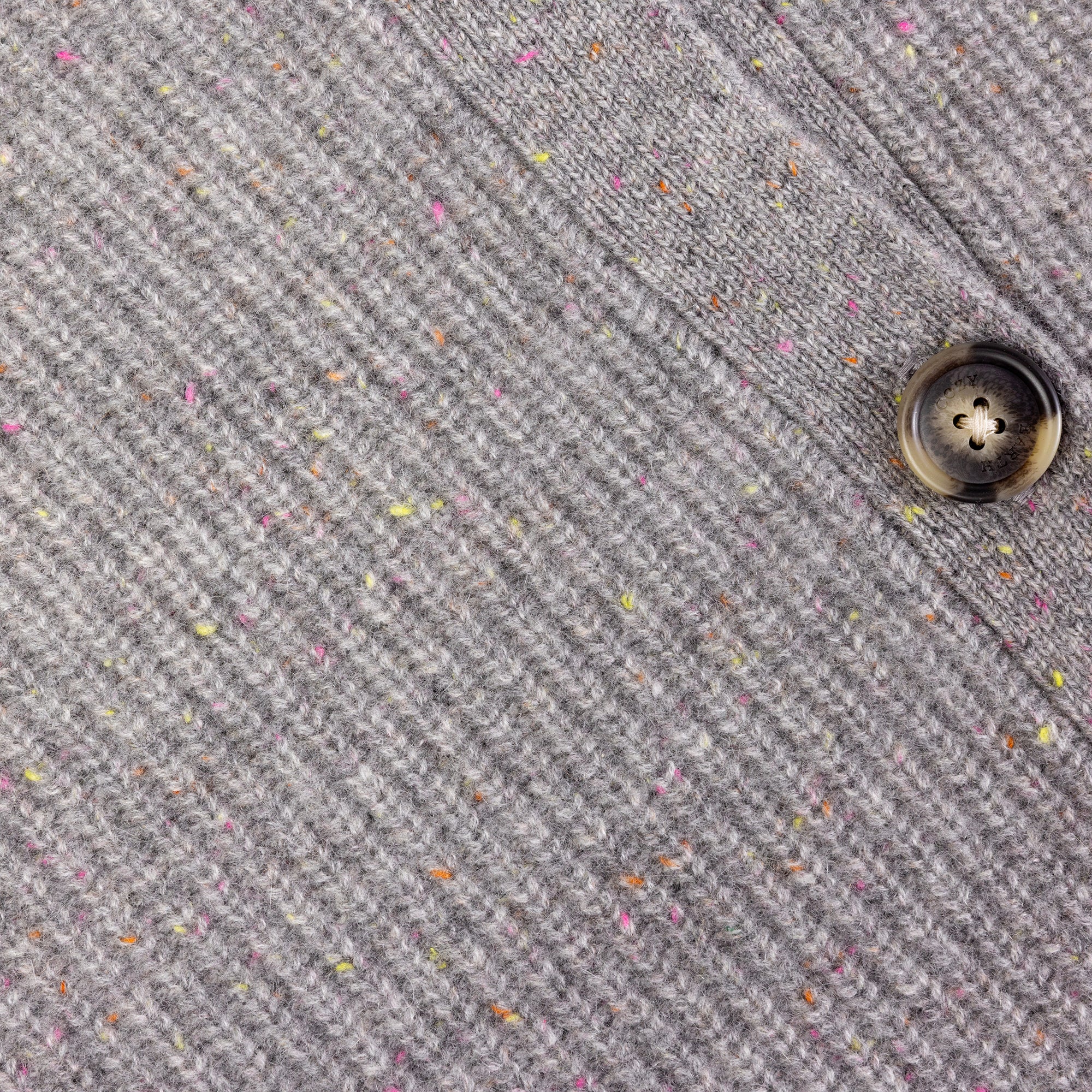 Close-up of a gray tweed fabric from the Oversized Sunday Cashmere Cardigan by Cozy Earth, showcasing its ribbed texture and multicolored specks. A single dark button is visible on the right side of the image, sewn onto the cardigan. 