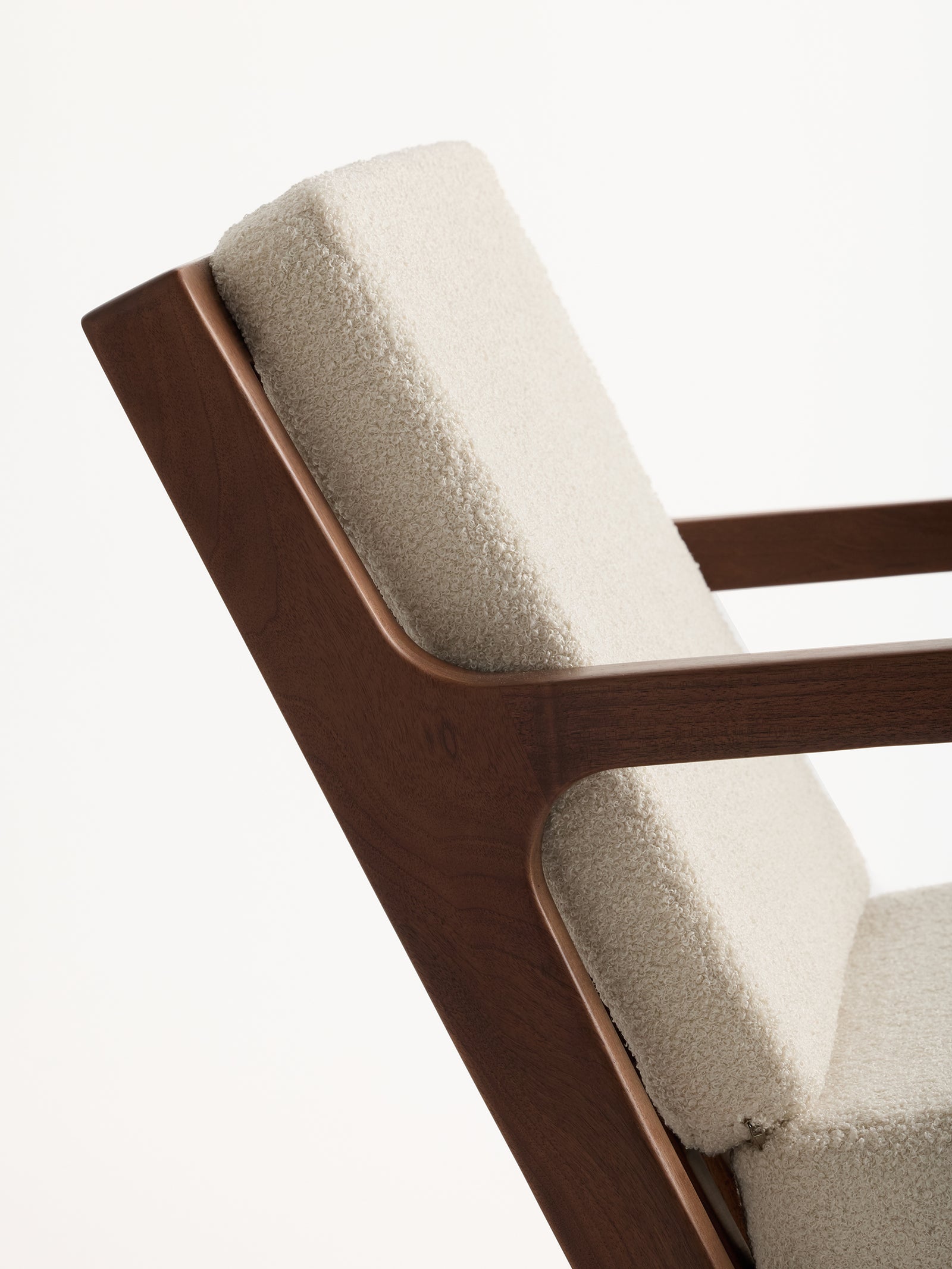 Close-up of the Coronado Lounge Chair by Cozy Earth, featuring a wooden frame and plush cream cushions. The chair is angled to showcase its sleek design and the soft texture of its upholstery against a plain background. 