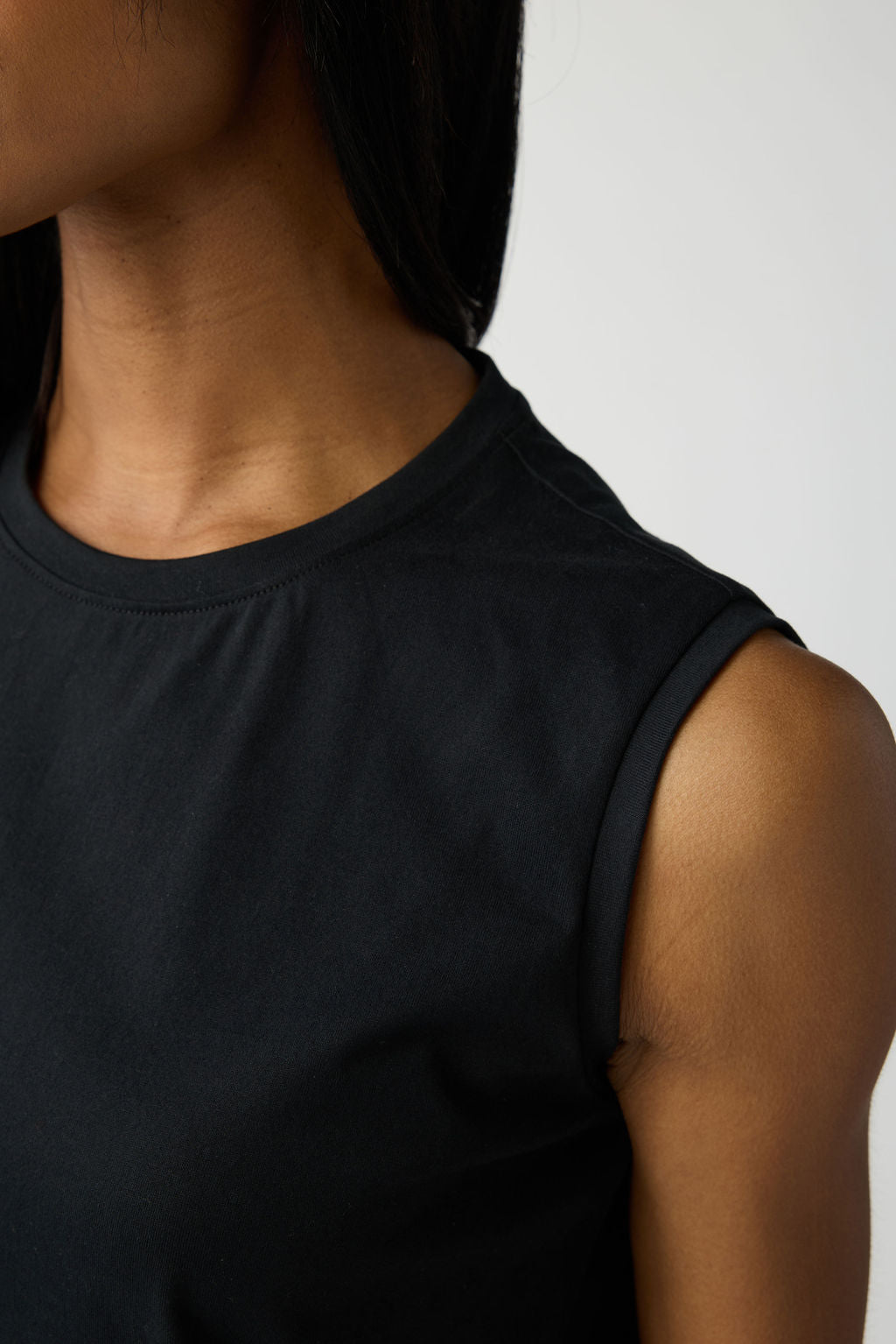 A closeup of the shoulder and neck of a woman wearing Cozy Earth All Day Sleeveless Tee in Jet Black. 