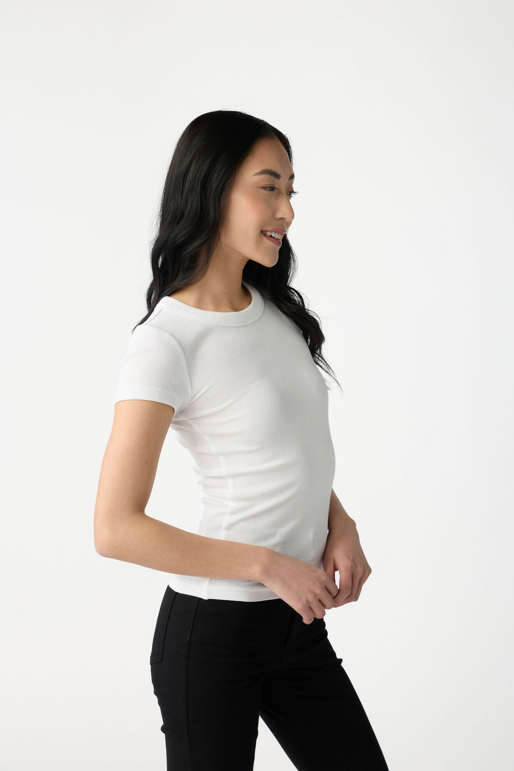 A dark haired woman wears Cozy Earth Women's Fine Ribbed Tee in White. She is turned to the side and pictured from the knees up. |Color:White