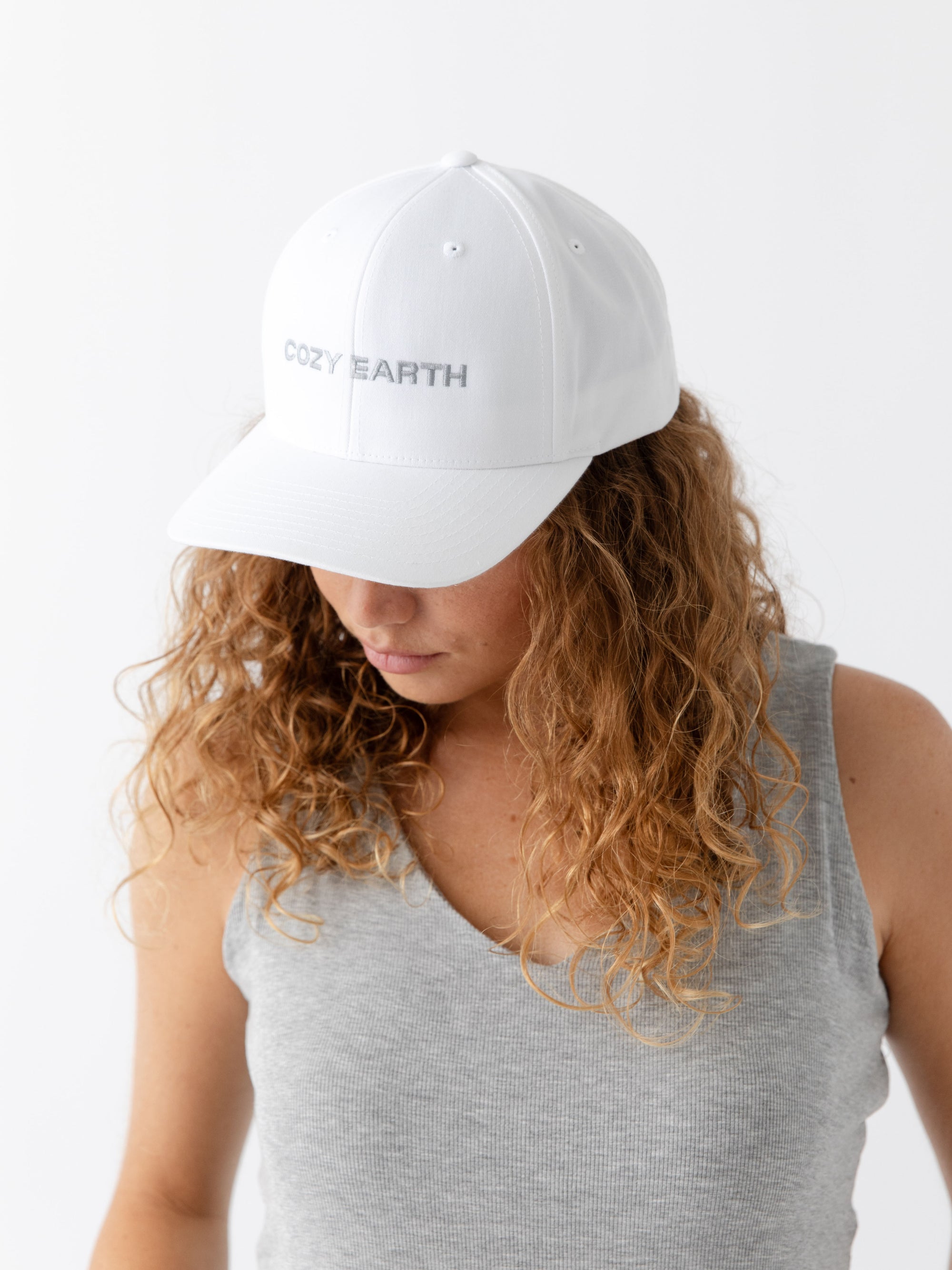 A woman wearing a White cap with 'COZY EARTH' text on a white background 