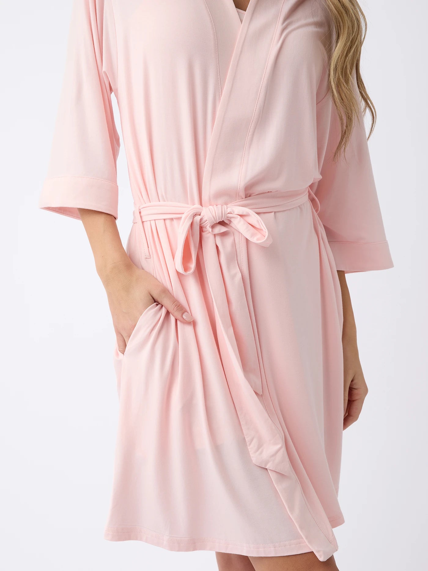 A person wears a Cozy Earth Women's Stretch-Knit Bamboo Kimono Robe in light pink, with 3/4 sleeves, a belt at the waist, and a pocket. The background is plain white. 