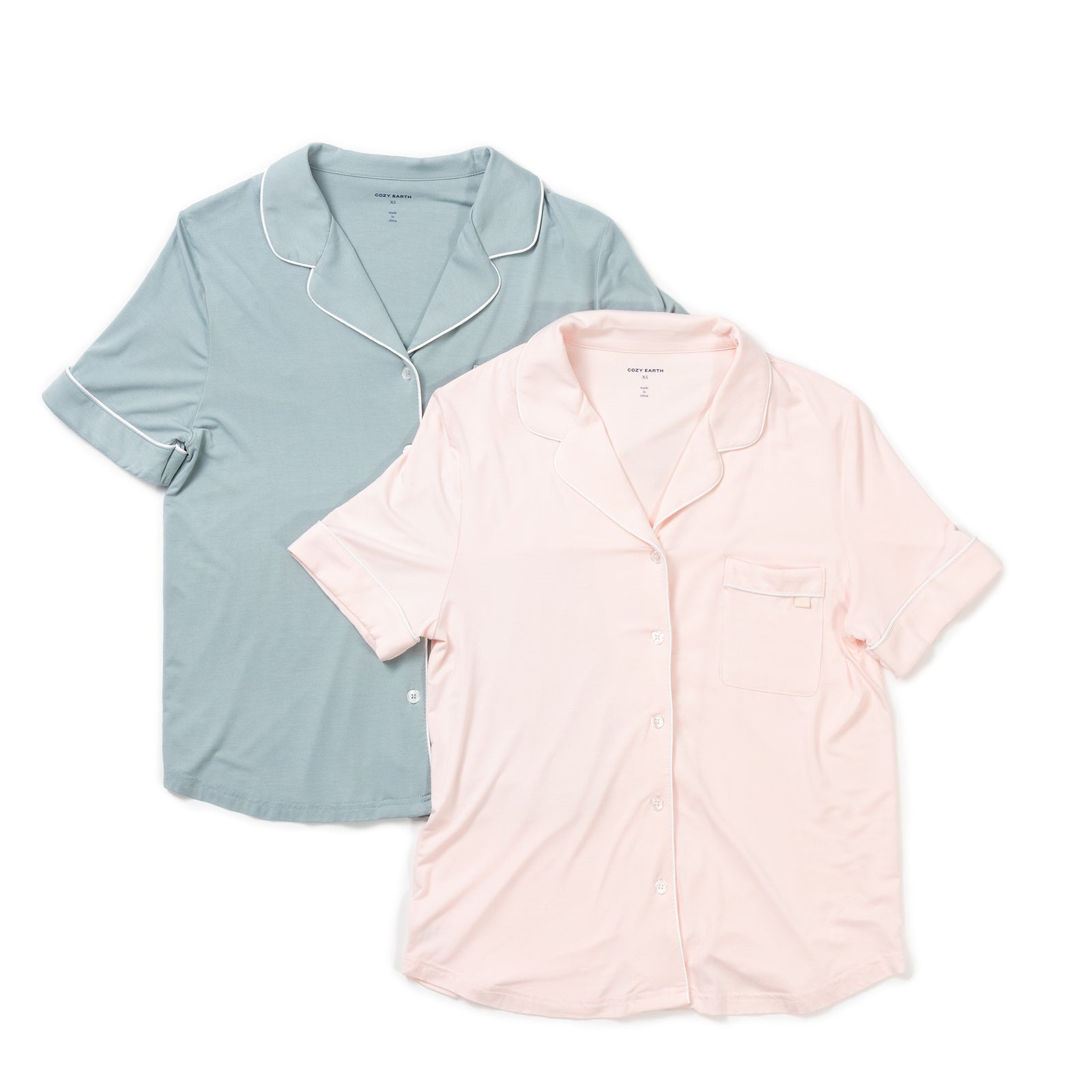 Two Women's Short Sleeve Bamboo Pajama Tops in Stretch-Knit from HIDE are laid out flat side by side. The one on the left is a pale blue with white piping along the collar and sleeves. The one on the right is light pink with matching piping details. Both tops have button-up fronts and chest pockets. 