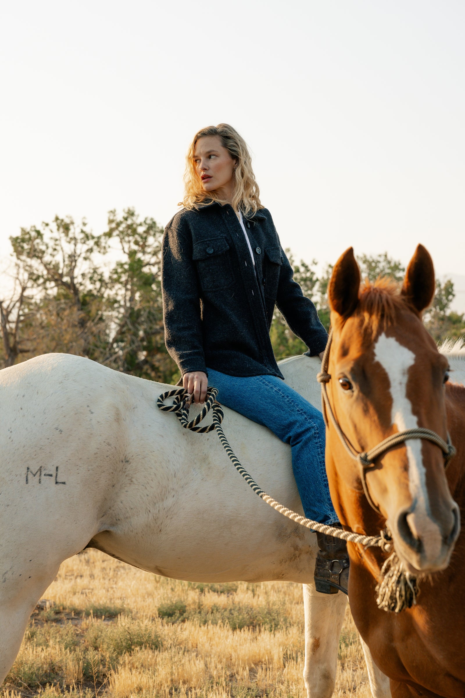 Woman in coal colored shacket riding white horse 