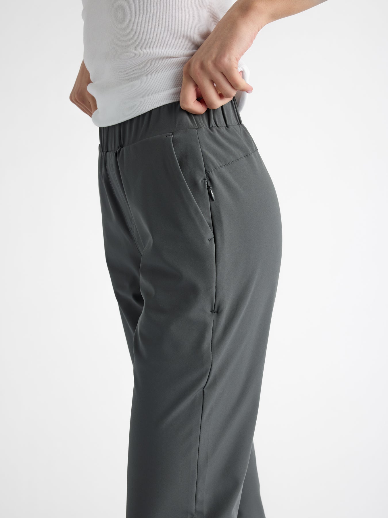 A person wearing Cozy Earth's Women's Always Cropped Pant in dark gray stands against a plain light background, with hands tucked into its elastic waistband. 