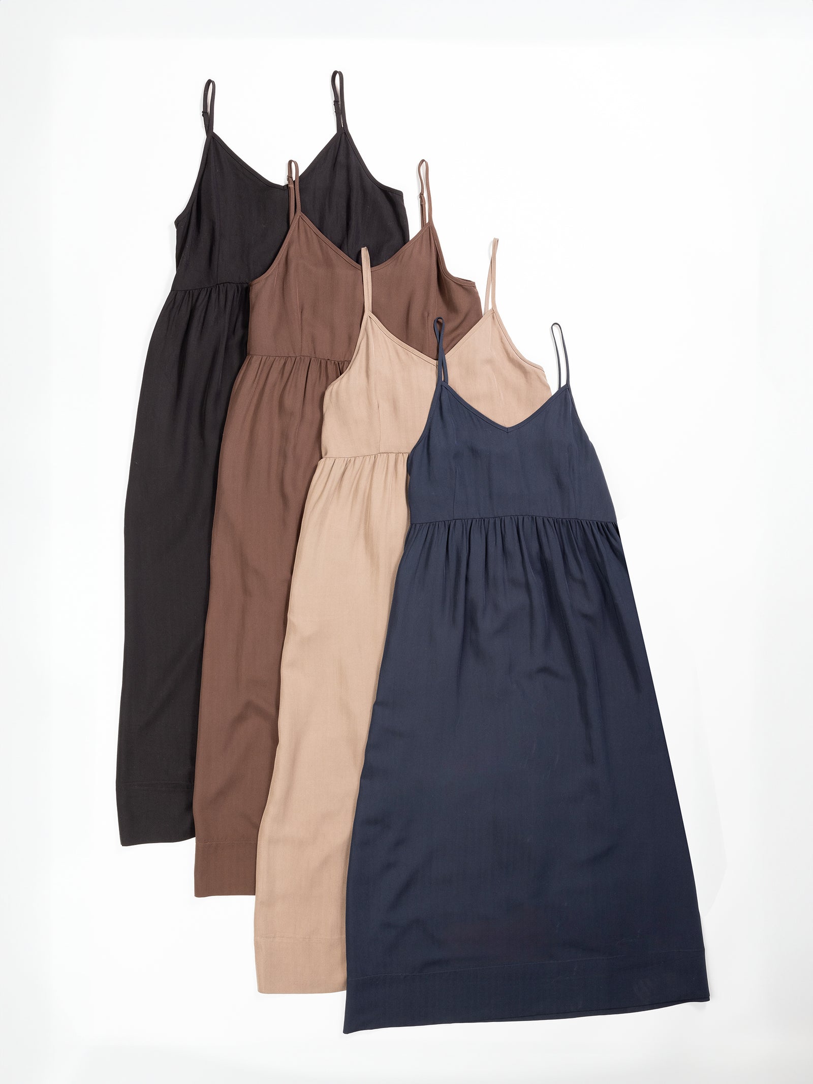 Four Cozy Earth Women's Sunset Gathered Dresses with spaghetti straps, arranged in a row on a white background. The dresses are in different colors: black, brown, beige, and dark blue. They feature a gathered waist and flowy skirts. 