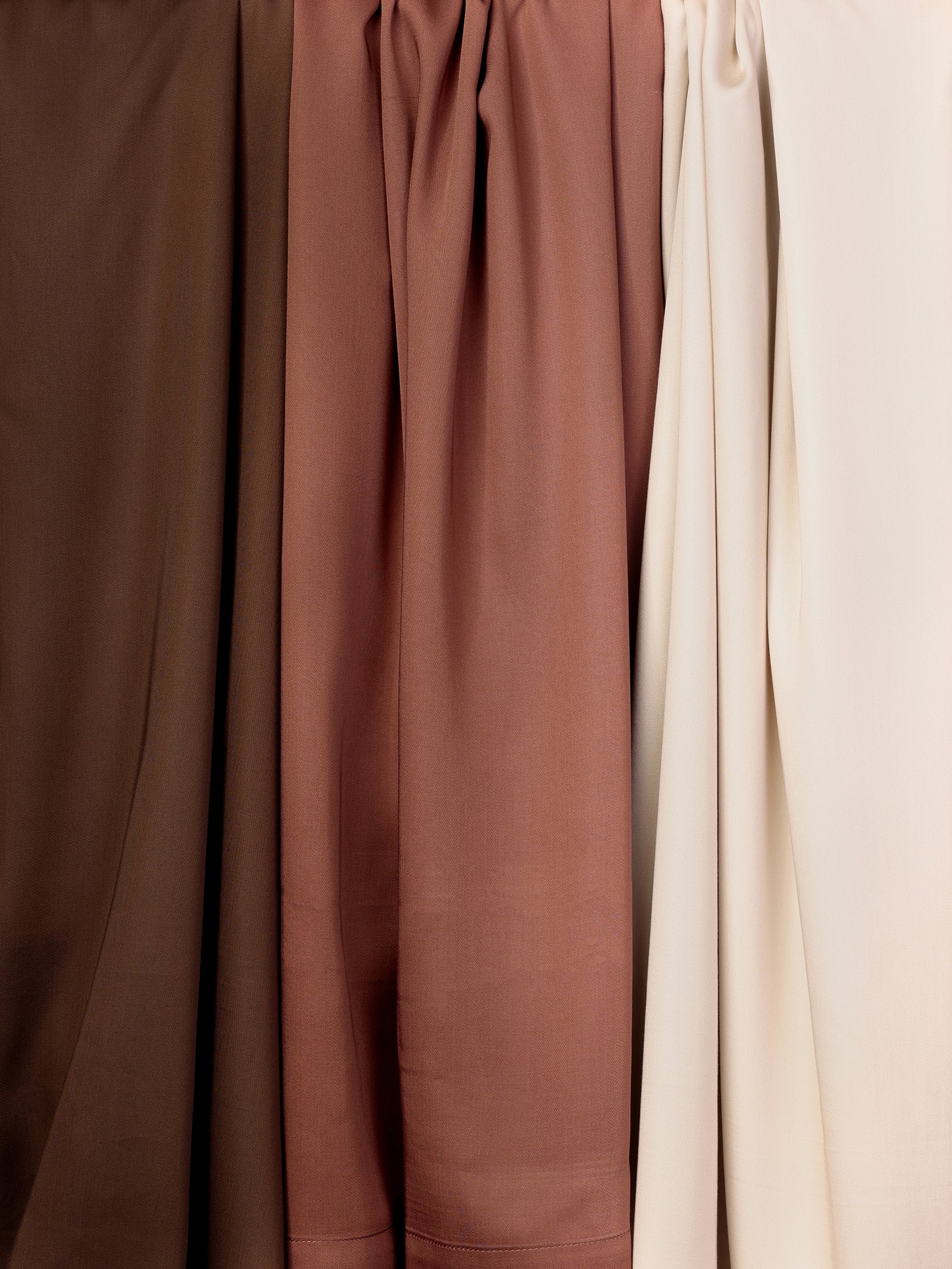 A row of hanging Bamboo Duvet Covers from Cozy Earth in various shades of brown and beige. The duvet covers are draped and gathered at the top, showcasing different textures and tones, ranging from dark brown on the left to light beige on the right. 