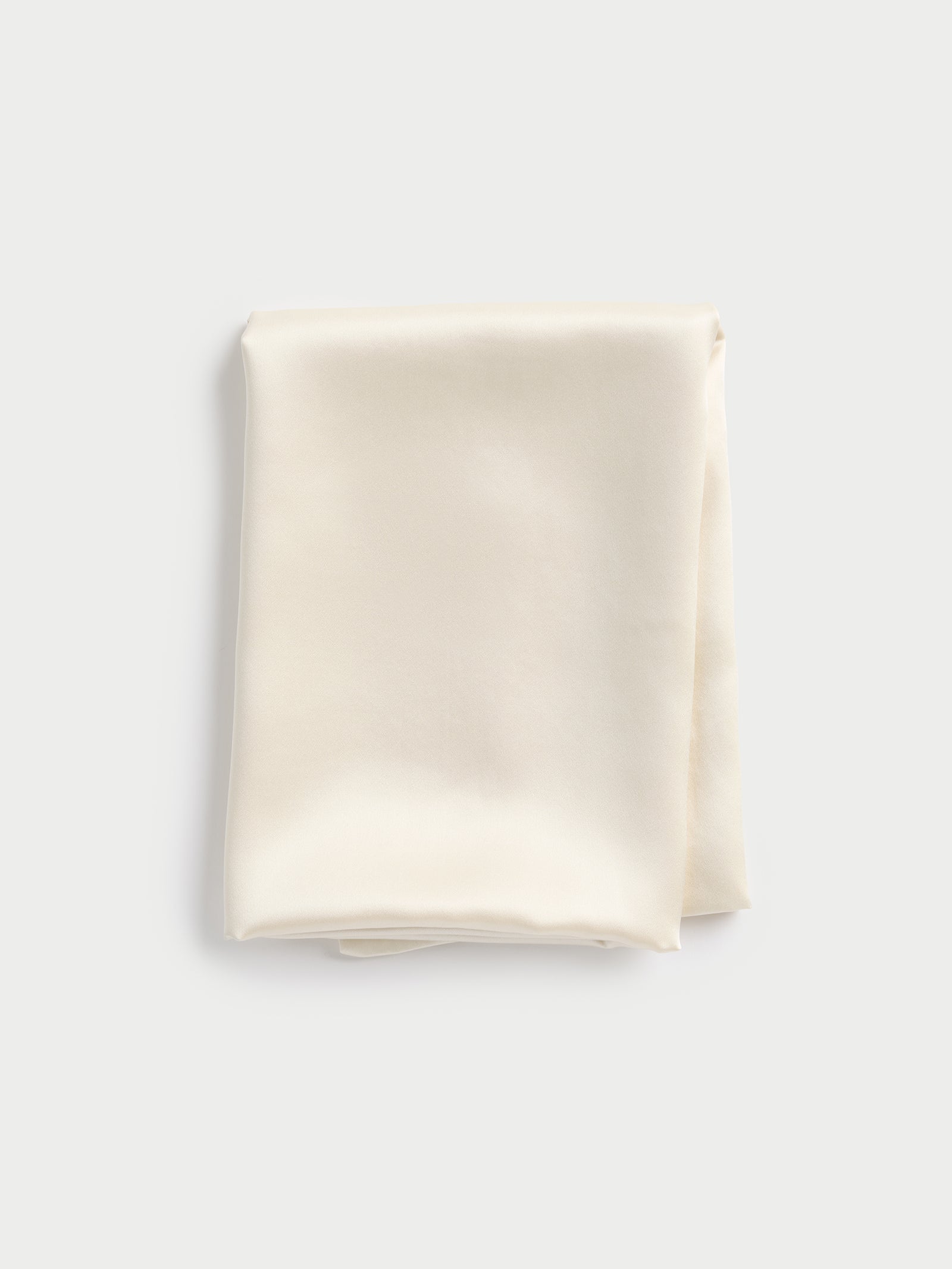 A neatly folded Silk Pillowcase by Cozy Earth, in a light cream tone, set against a plain background. The pillowcase features a soft sheen that highlights its smooth texture. 