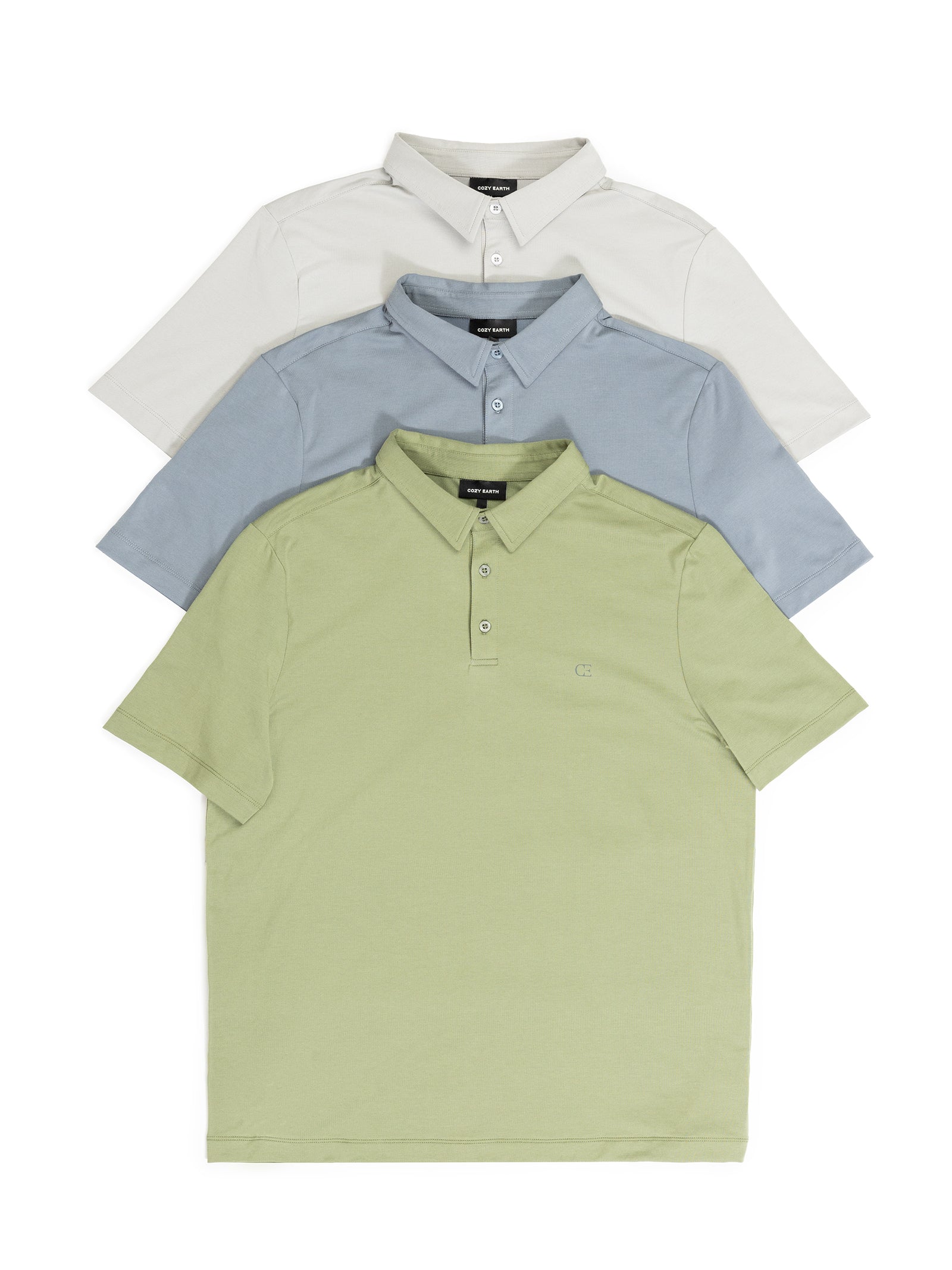 A stack of three neatly folded polo shirts in pastel shades from Cozy Earth's Men's Everyday Polo collection is displayed. The top shirt is off-white, the middle one is light blue, and the bottom shirt is light green. Each shirt features a small embroidered logo on the chest. 