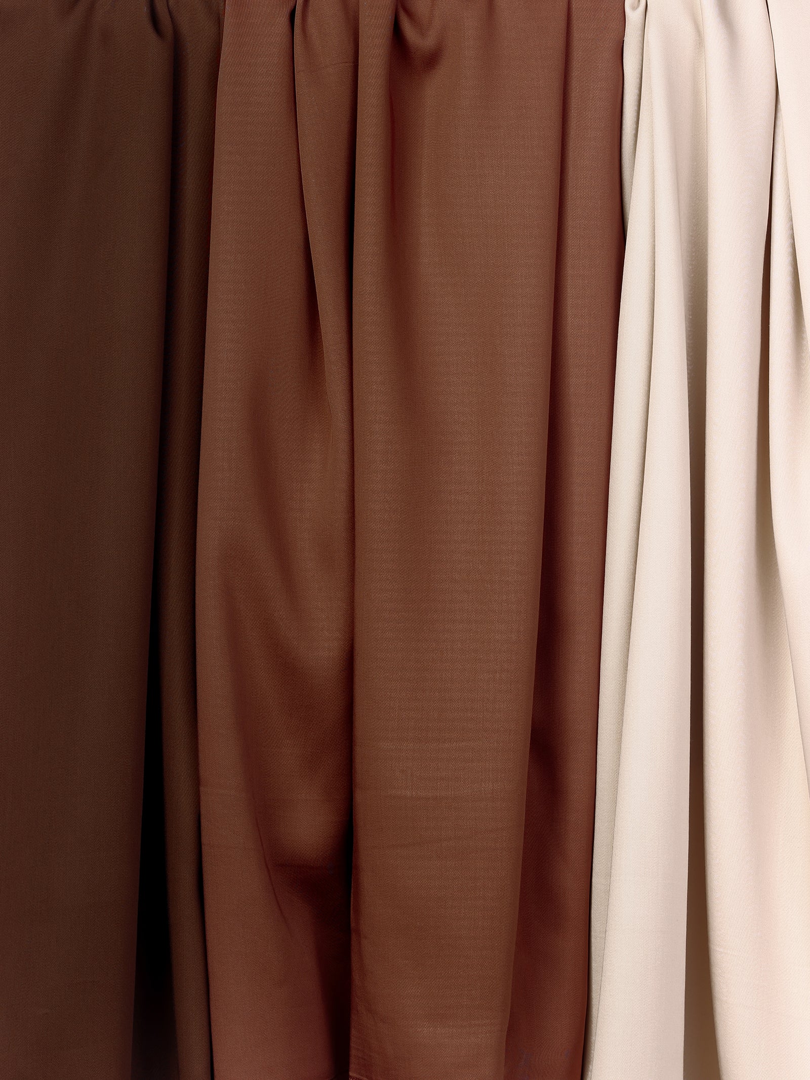 A row of hanging Bamboo Duvet Covers from Cozy Earth in various shades of brown and beige. The duvet covers are draped and gathered at the top, showcasing different textures and tones, ranging from dark brown on the left to light beige on the right. 