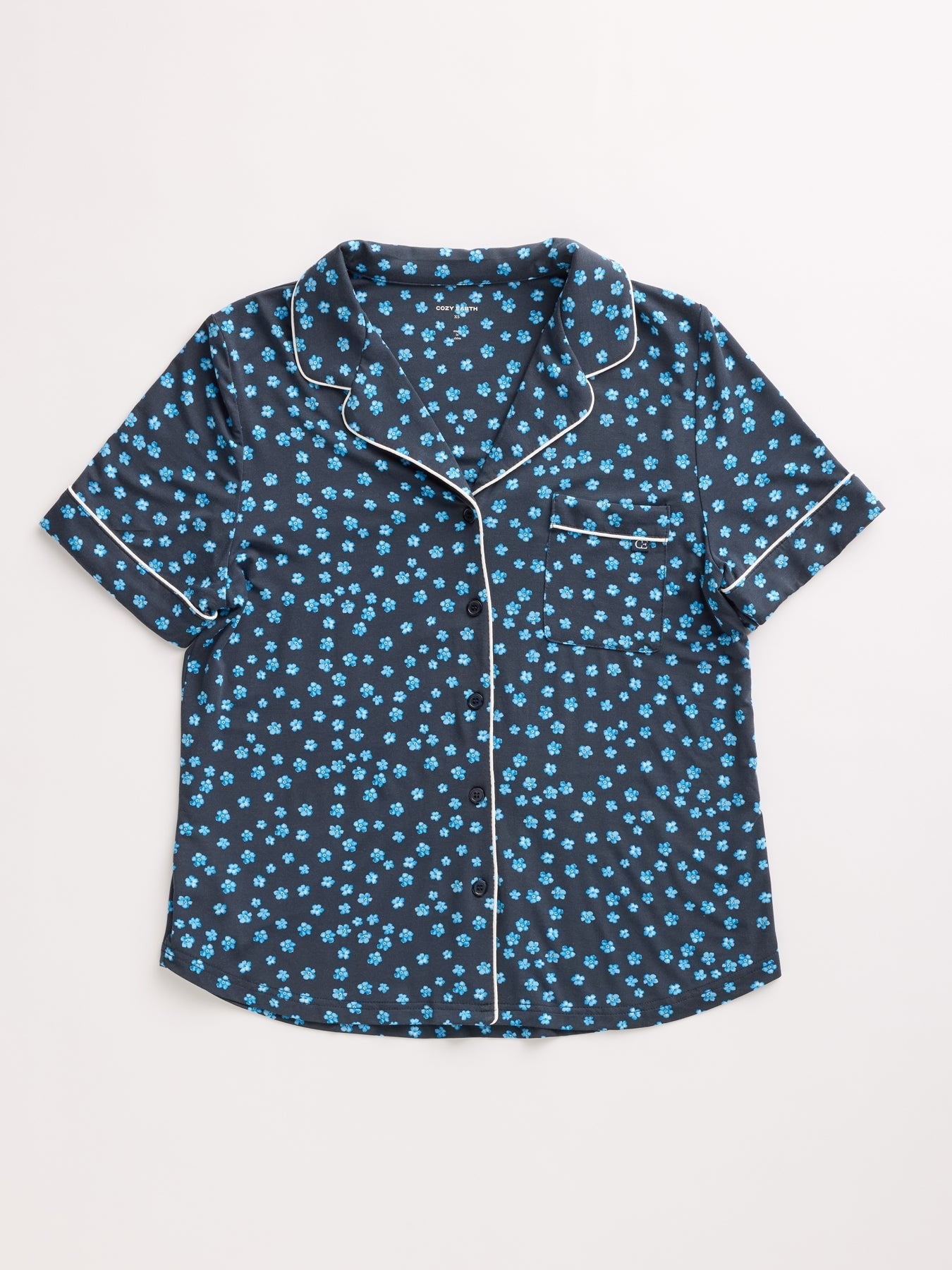 The Women's Bamboo Stretch-Knit Short Sleeve Pajama Top by HIDE is navy with a small blue floral pattern, featuring white piping on the collar, button line, cuffs, and chest pocket. 