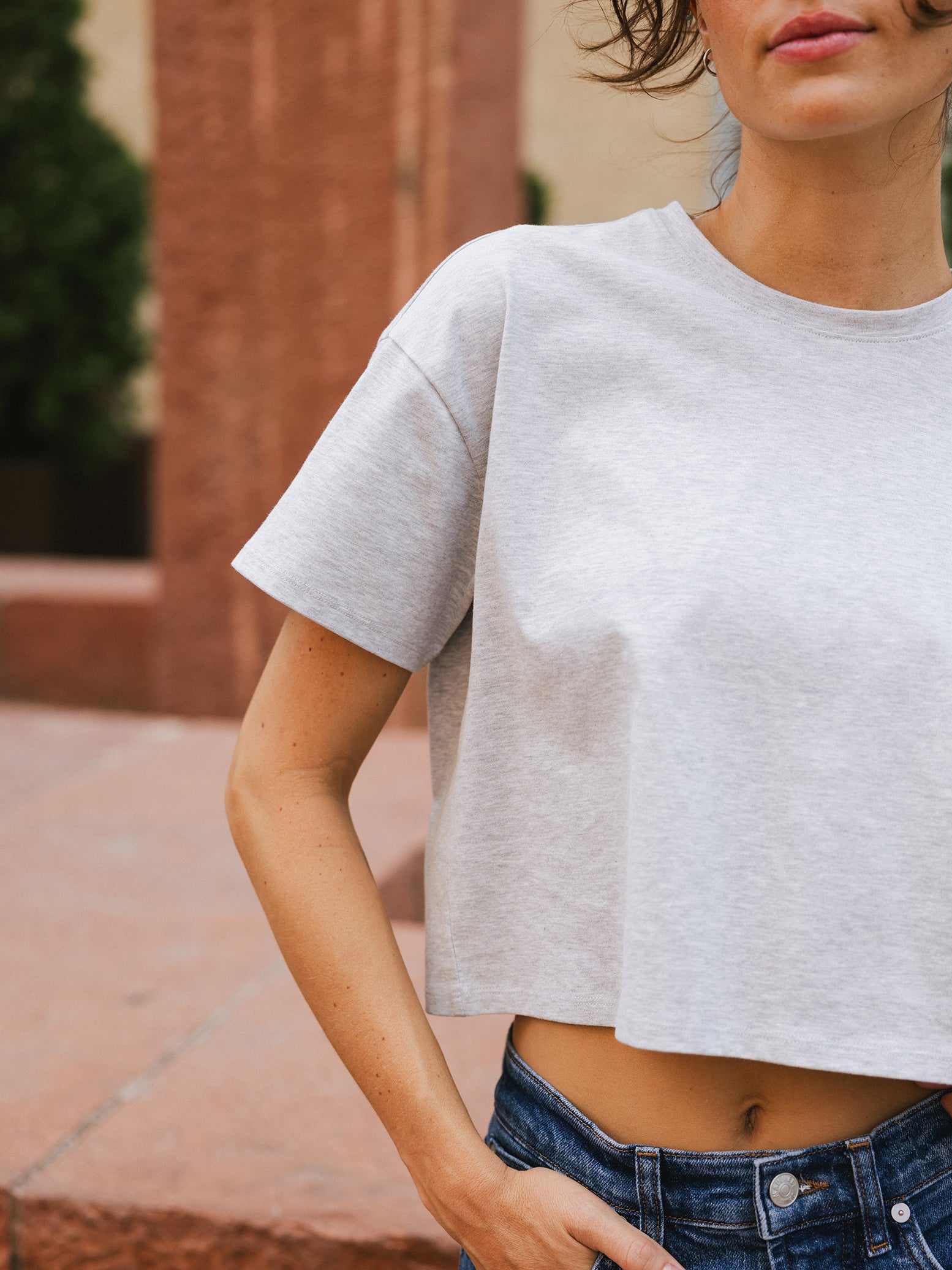 French Dove Heather All Day Cropped Tee. The photo of the All Day Cropped Tee is taken with a with a city background and is worn by a woman. 