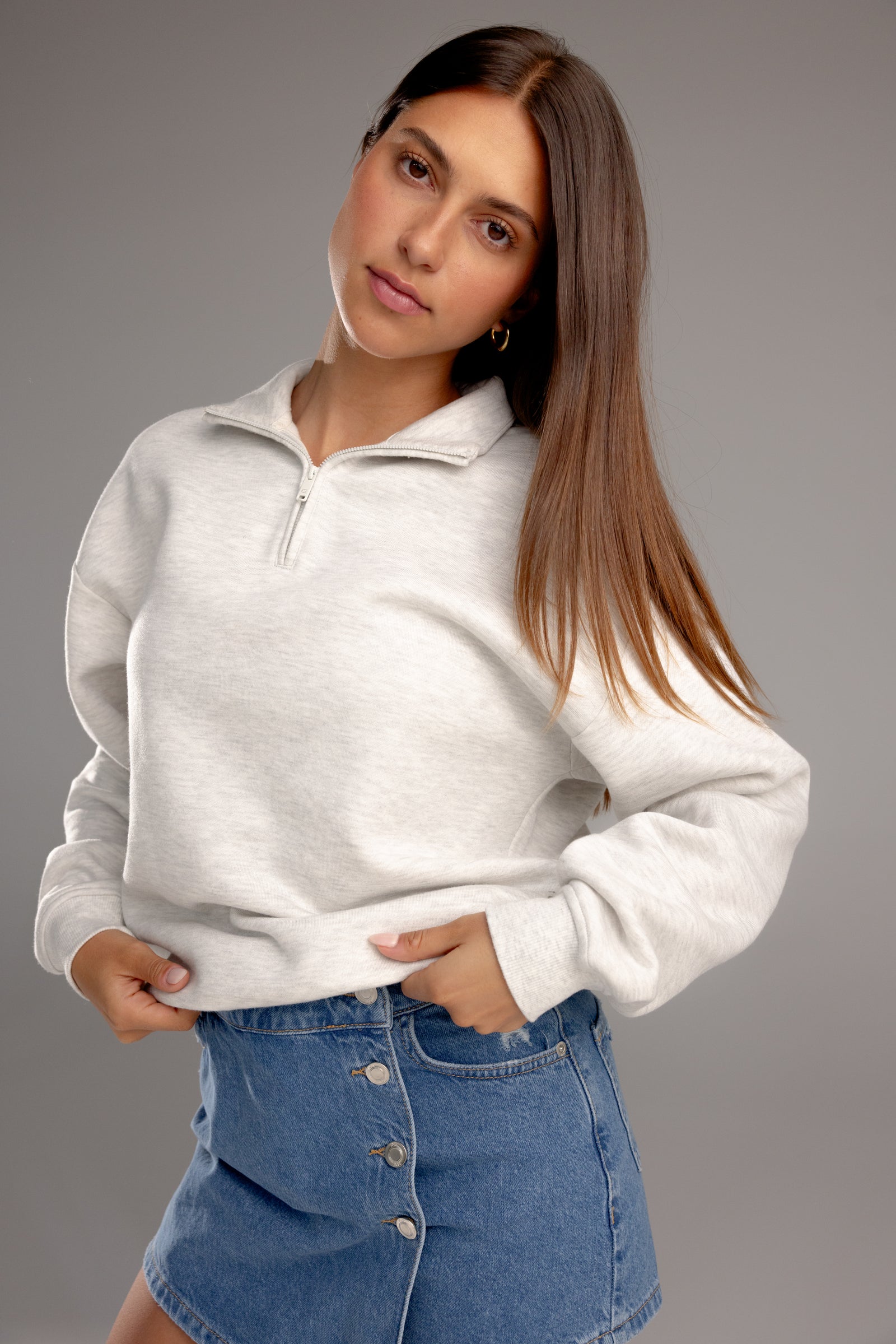 Heather Grey CityScape Quarter Zip. The quarter zip is being worn by a female model. The model is wearing an accompanying jean skirt to complete the look of the quarter zip. The photo was taken with a grey background. 