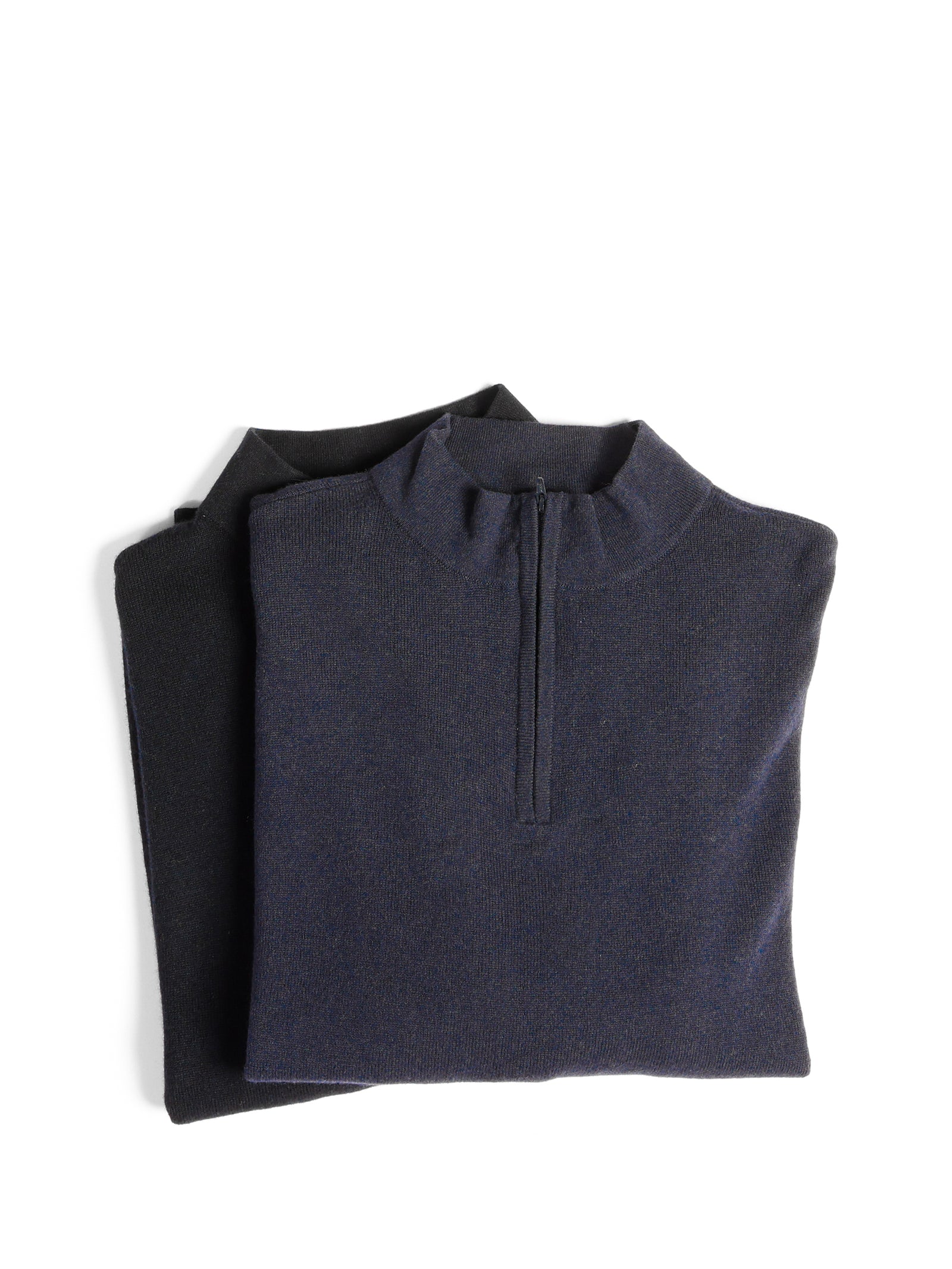 Two folded sweaters are stacked on top of each other against a white background. The top one is a navy blue Men's Quarter Zip Sweater from Cozy Earth, while the bottom one is dark gray and barely visible beneath the blue sweater. 