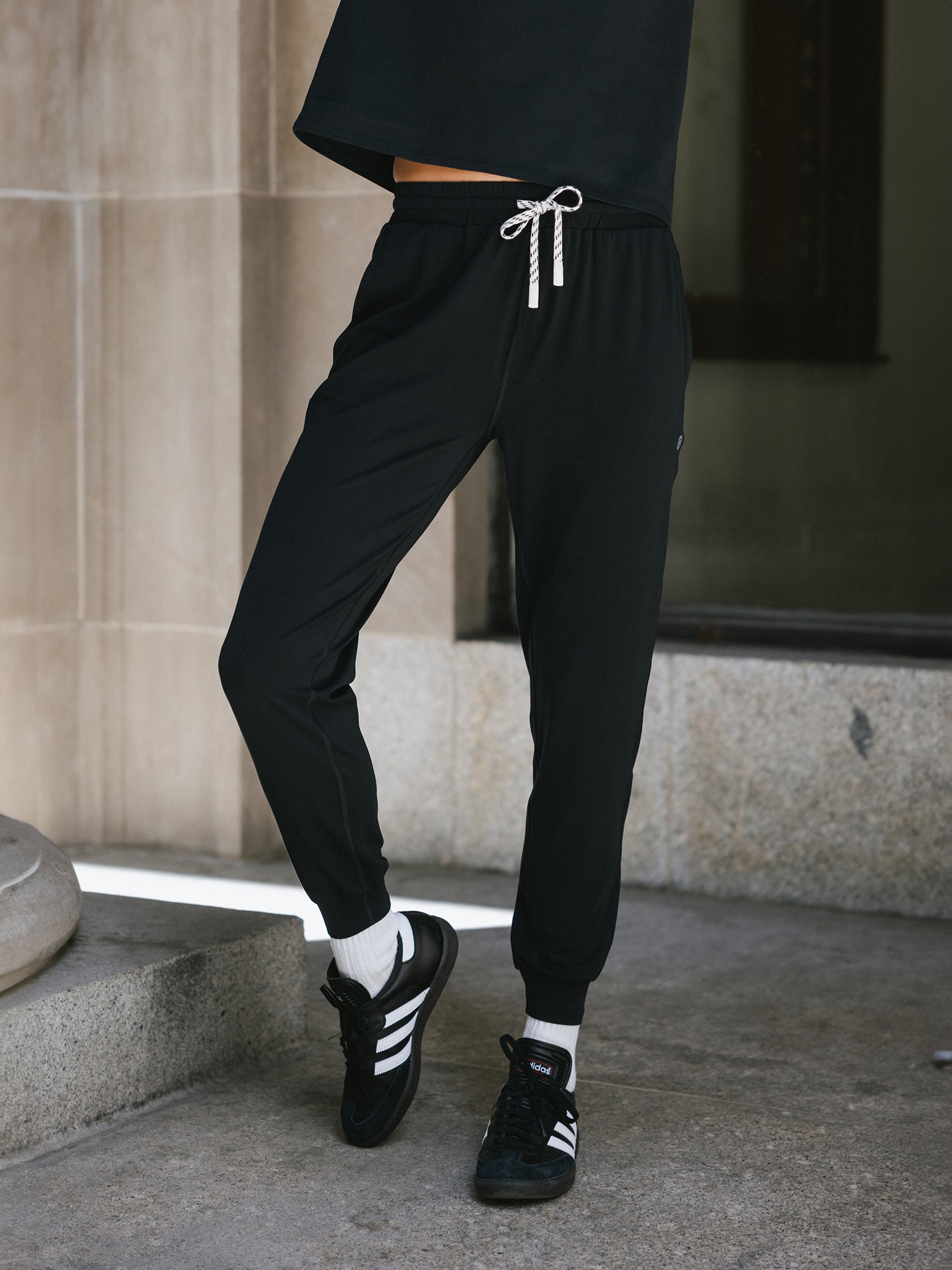 Jet Black Studio Jogger. The Studio Joggers are worn by a woman photographed with a city type background. 