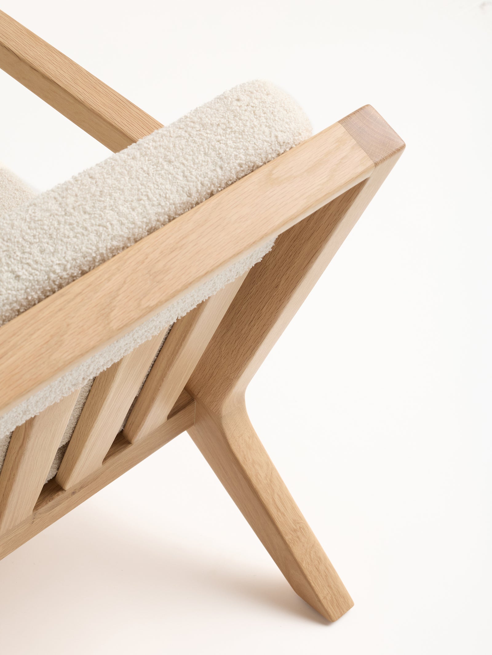 A close-up of Cozy Earth's Coronado Lounge Chair showcasing a modern design with an angled frame. The chair is adorned with a plush, off-white cushion and boasts a natural wood finish. Its frame forms geometric shapes, reflecting excellent craftsmanship and style. 