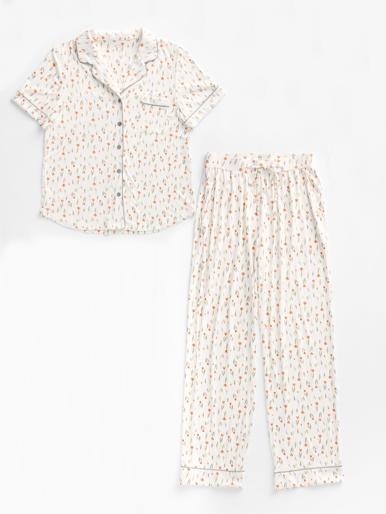 The Women's Bamboo Stretch-Knit Short Sleeve & Pant Pajama Set by Cozy Earth features a short-sleeve button-up top with chest pocket and long pants. It has a white background with small red and green leaf pattern, complemented by white trim. 