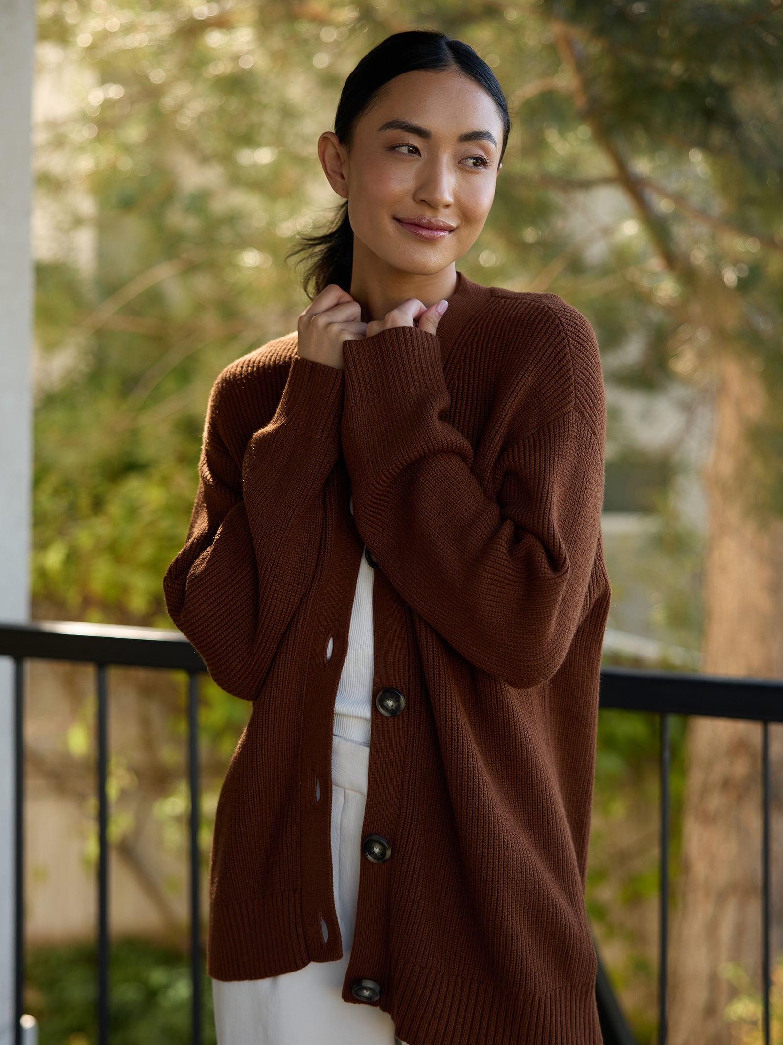 Woman in Oversized Classic Cardigan - Spice with trees in the background. 